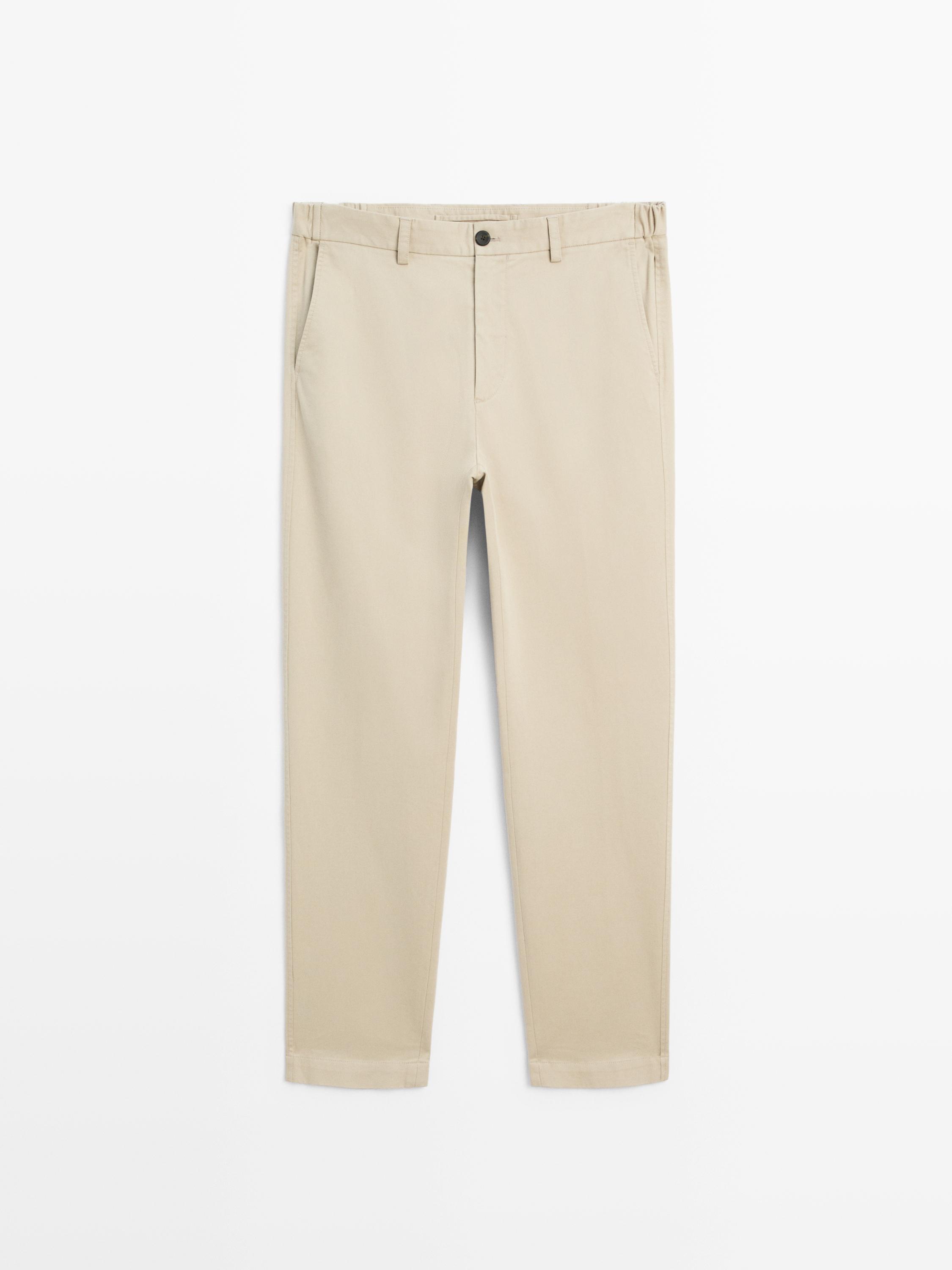 Vista frontal de pantalón beige slim fit con bolsillos laterales y botón frontal negro.