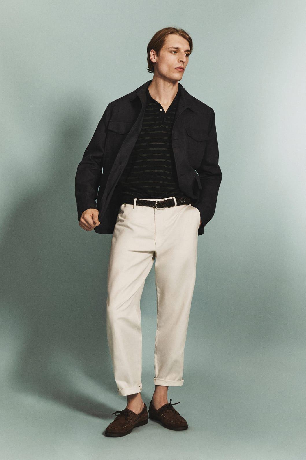 Jaka beltza, polo marraduna, praka beixak eta mokasin marroiak dituen modeloa, hondo urdin argiaren gainean.