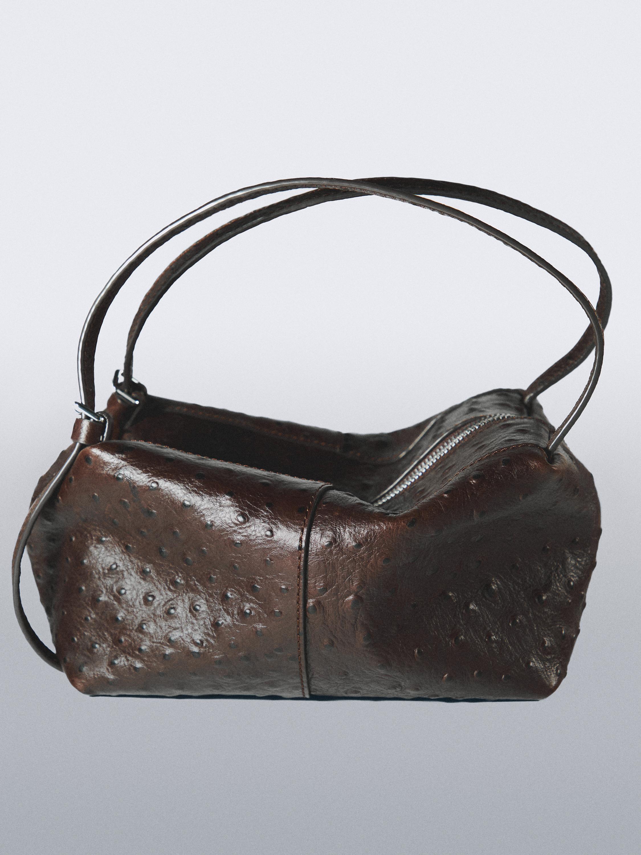 "Vista lateral de bolso marrón con textura y cierre de cremallera, asas dobles y forma rectangular."