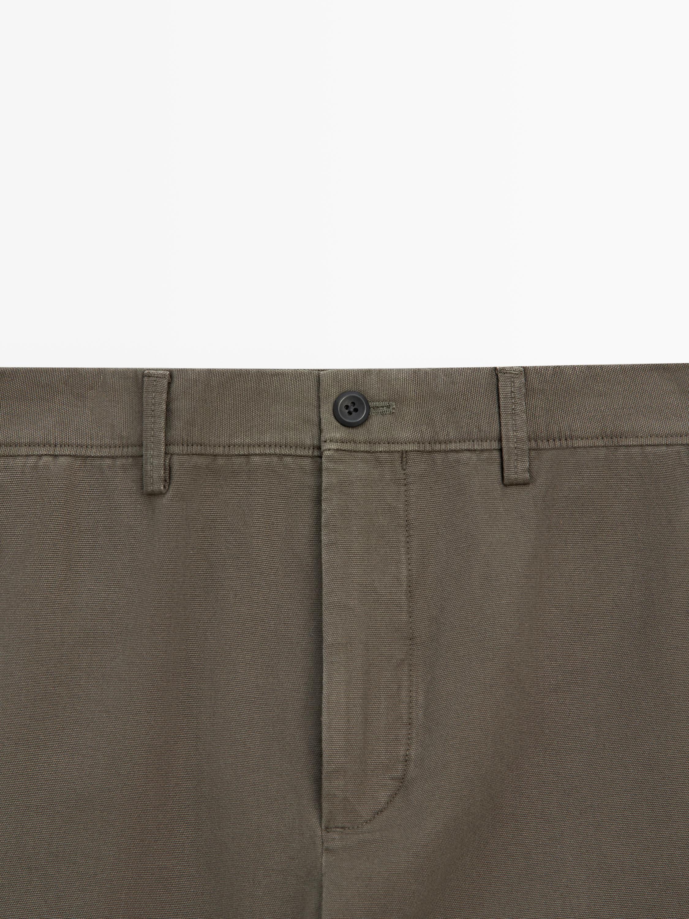 Plano medio de la cintura de un pantalón verde con botón negro y trabillas para cinturón.