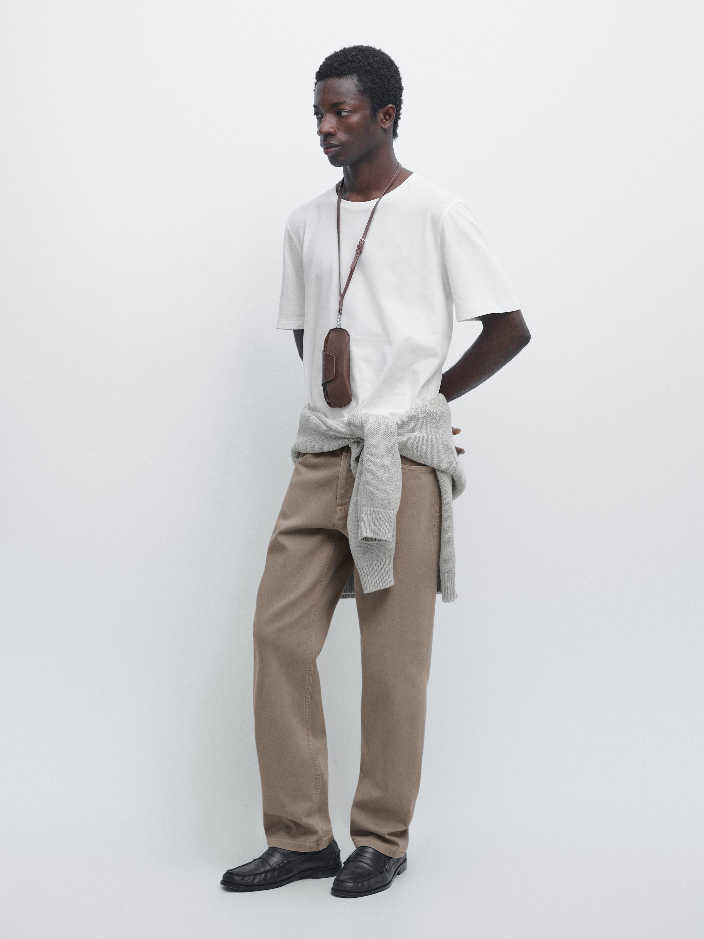 Conjunto de camiseta blanca de manga corta, pantalones beige, suéter gris atado a la cintura y zapatos negros.