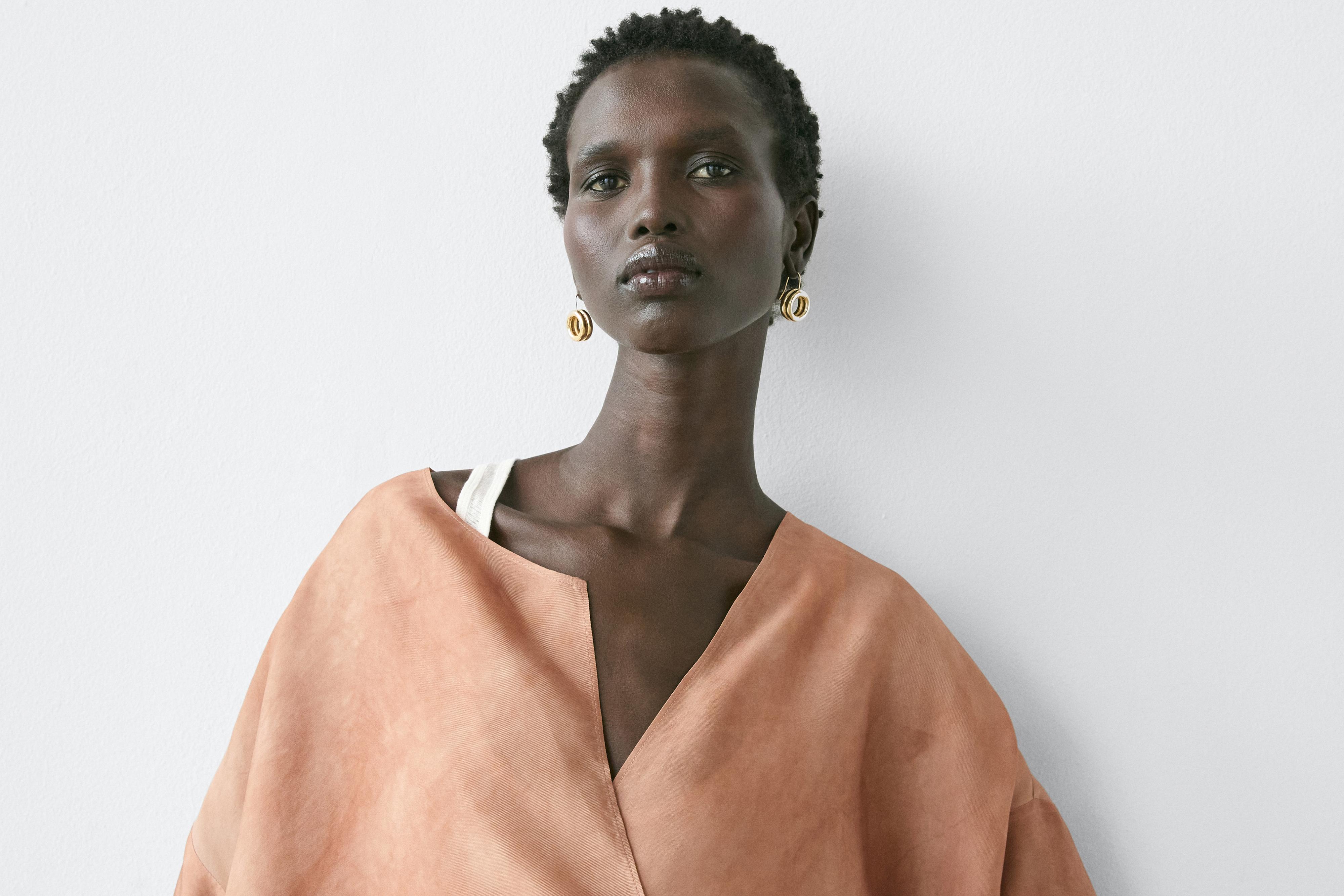 "Plano medio de camisa beixe con escote en V e ombreiro caído."