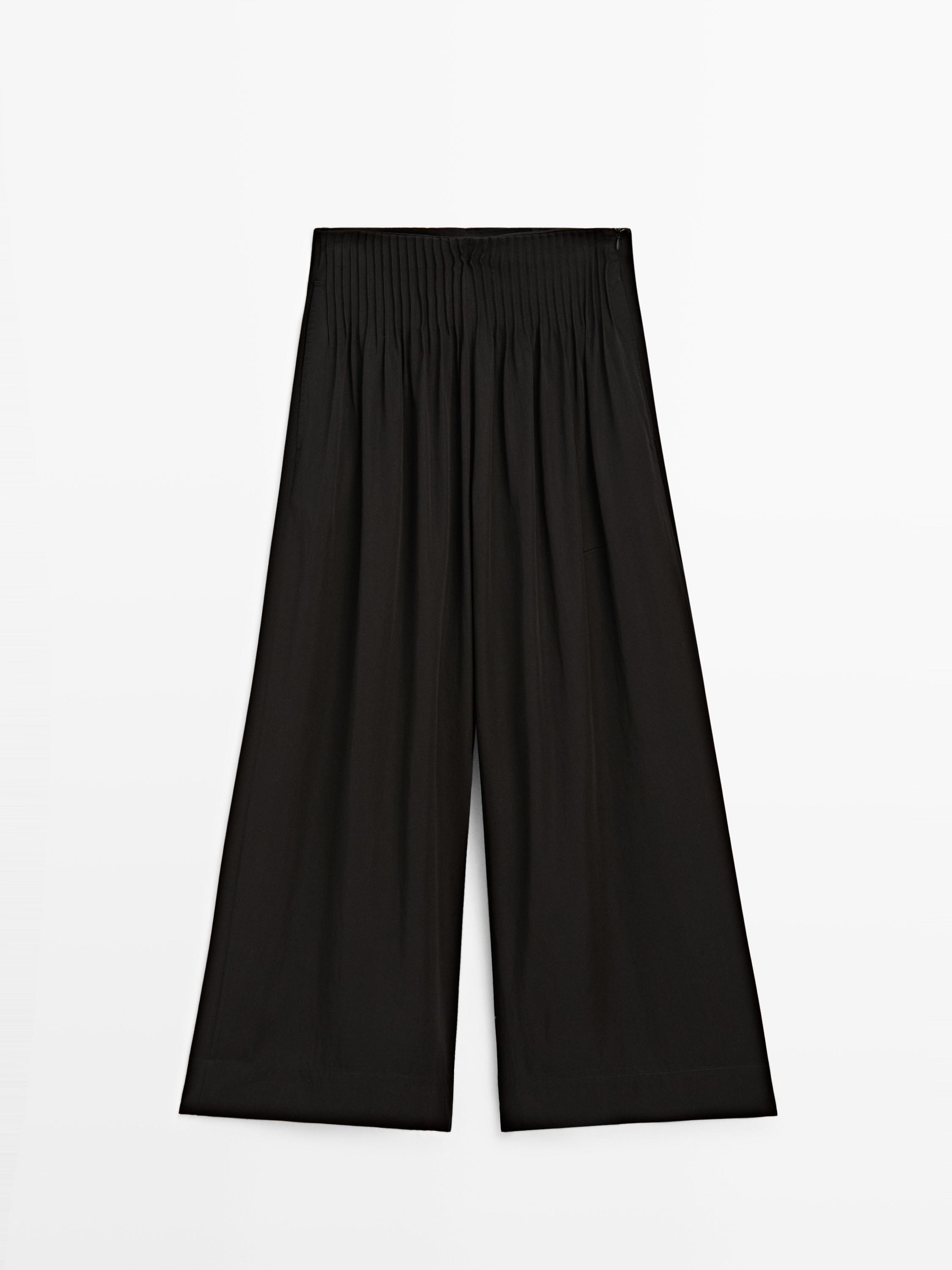 Front view of wide, flowing black pants with an elastic waistband and pleats.