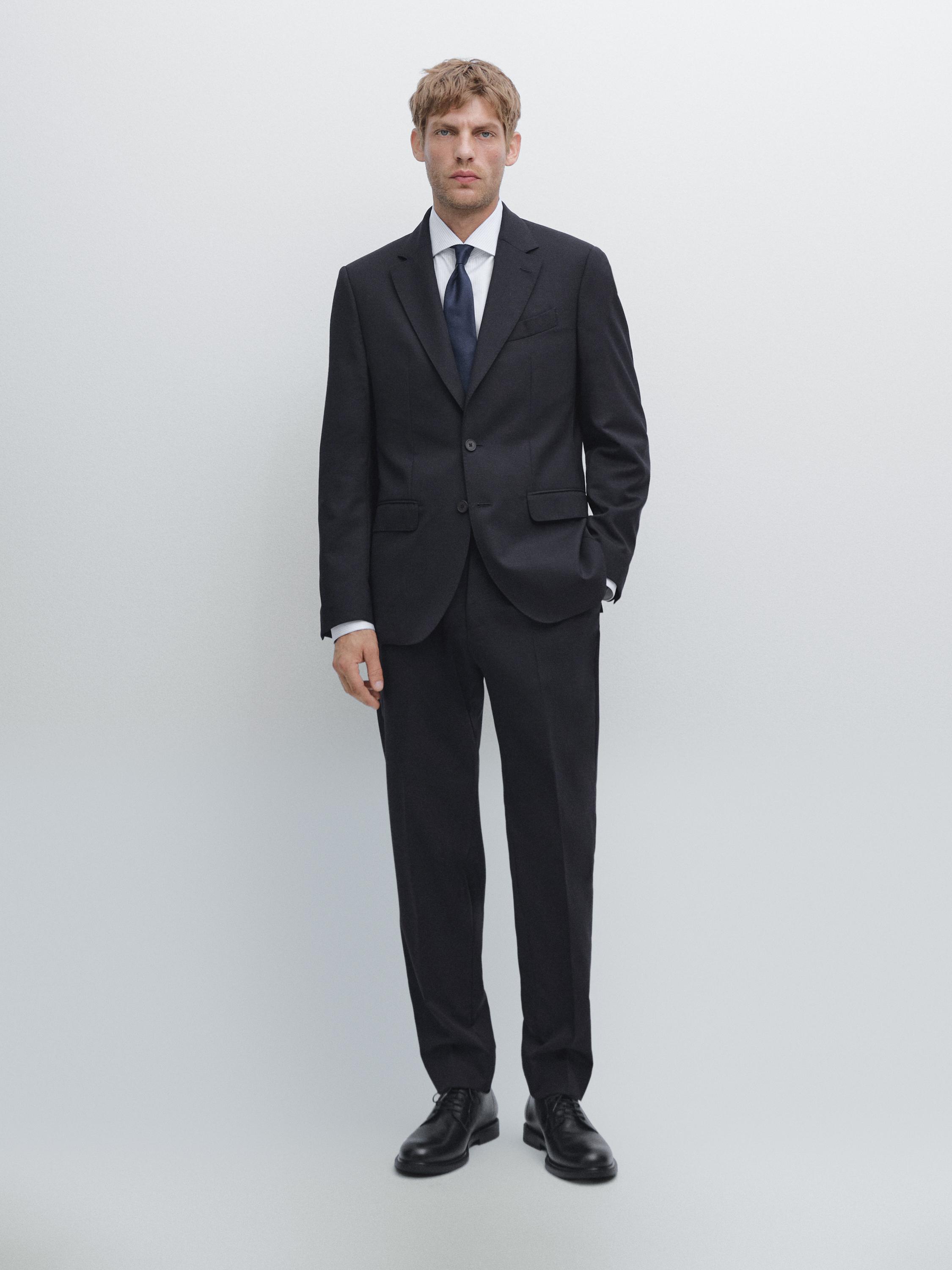 Ensemble de costume bleu marine avec veste deux boutons, poches à rabat et pantalon droit. Chemise blanche et cravate bleue.