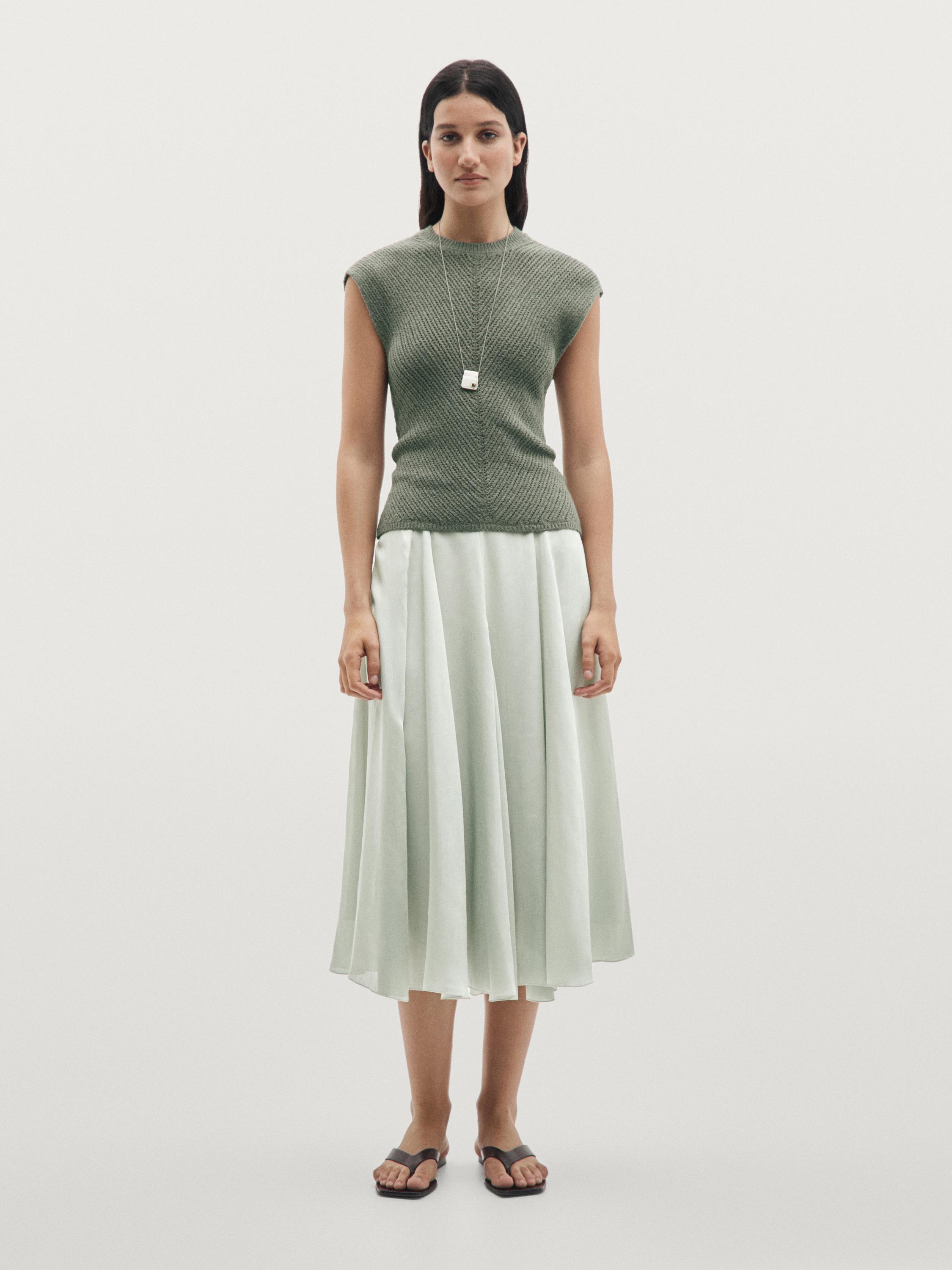 Conjunto de top verde azul sin mangas con detalles calados y falda larga plisada en tono claro.