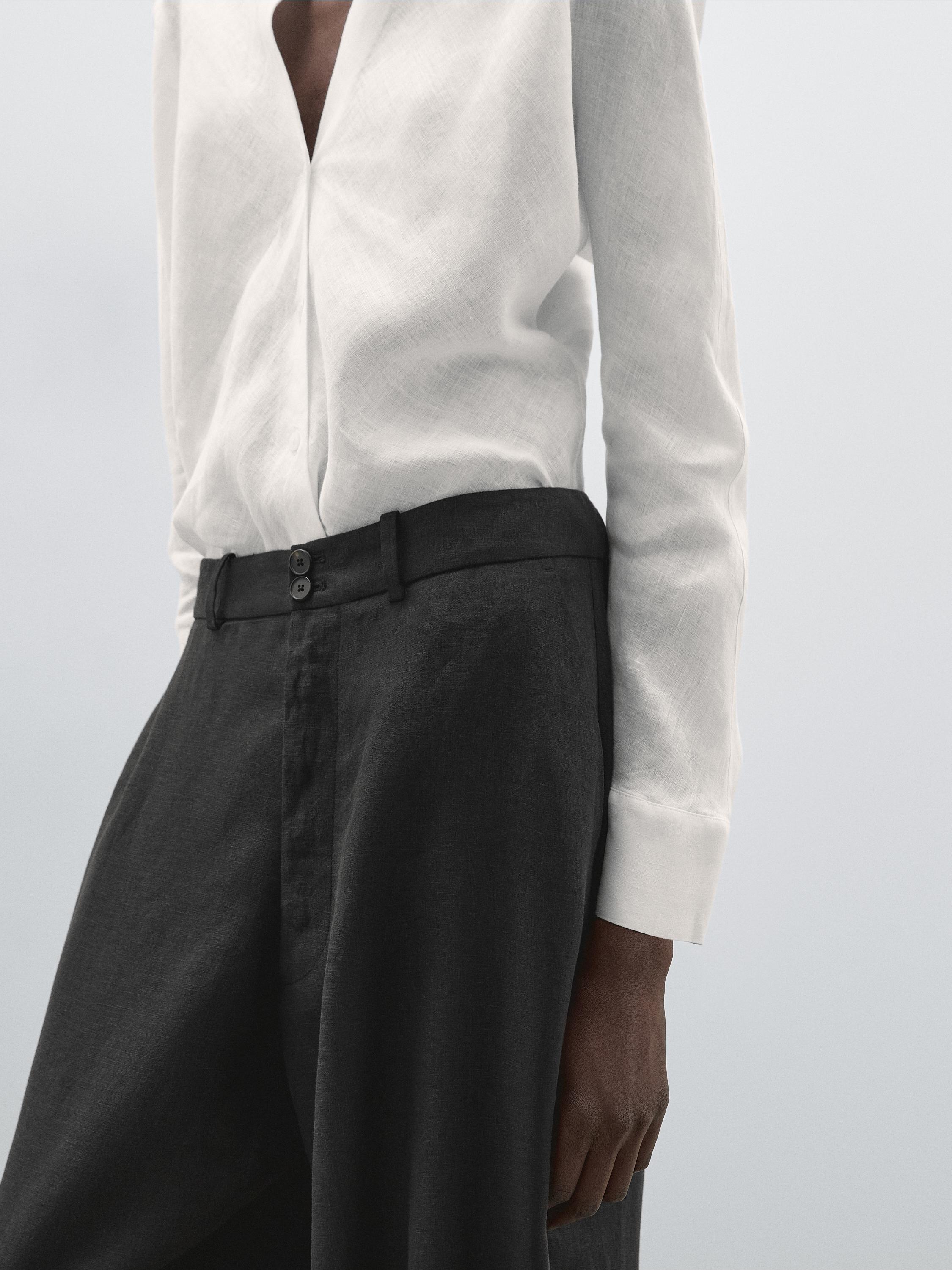 لقطة متوسطة لقميص أبيض مفتوح وبنطلون أسود بأزرار أمامية.