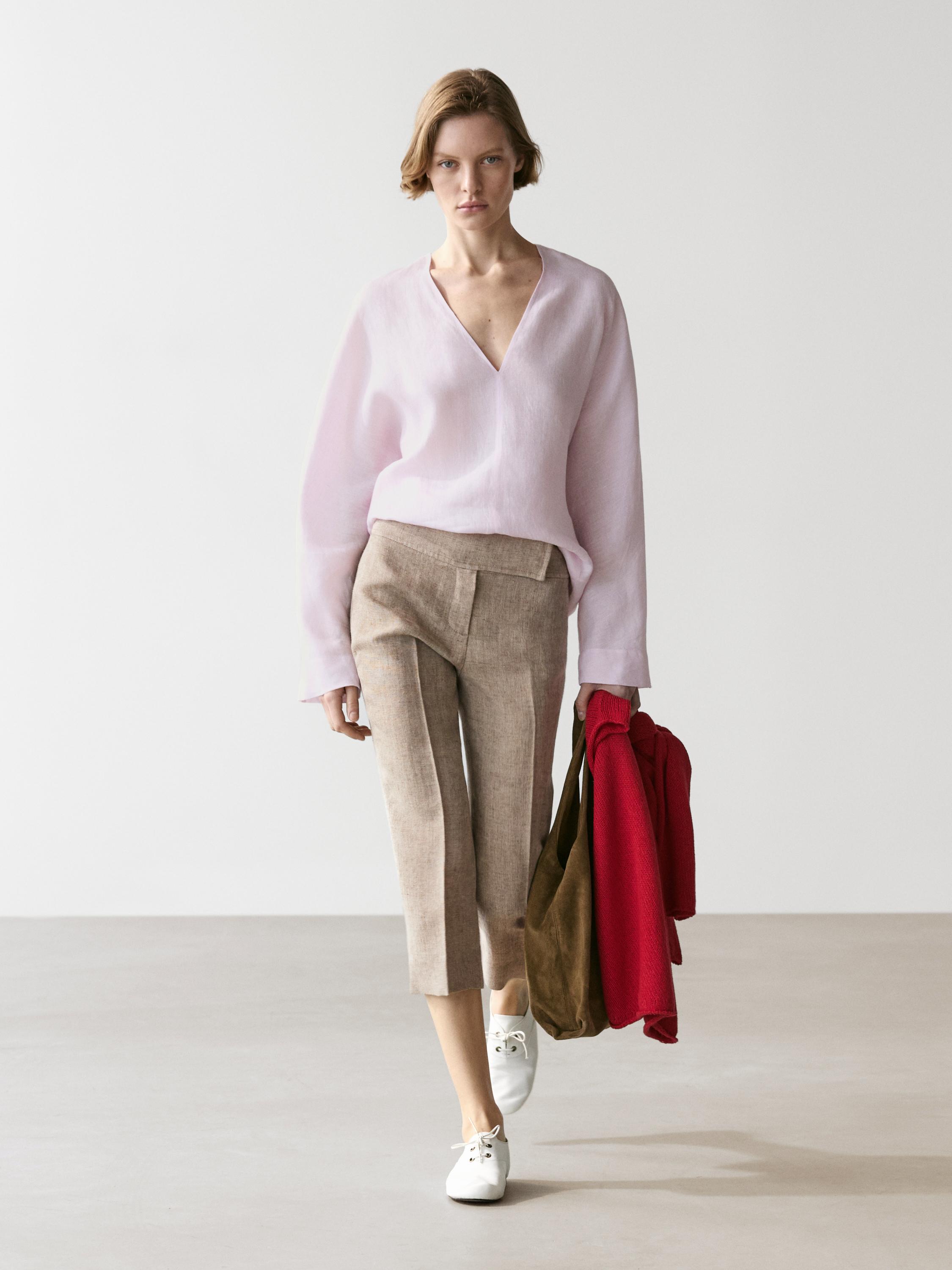 Conjunto de blusa rosa de cuello pico y pantalones beige de corte recto, con zapatos blancos.