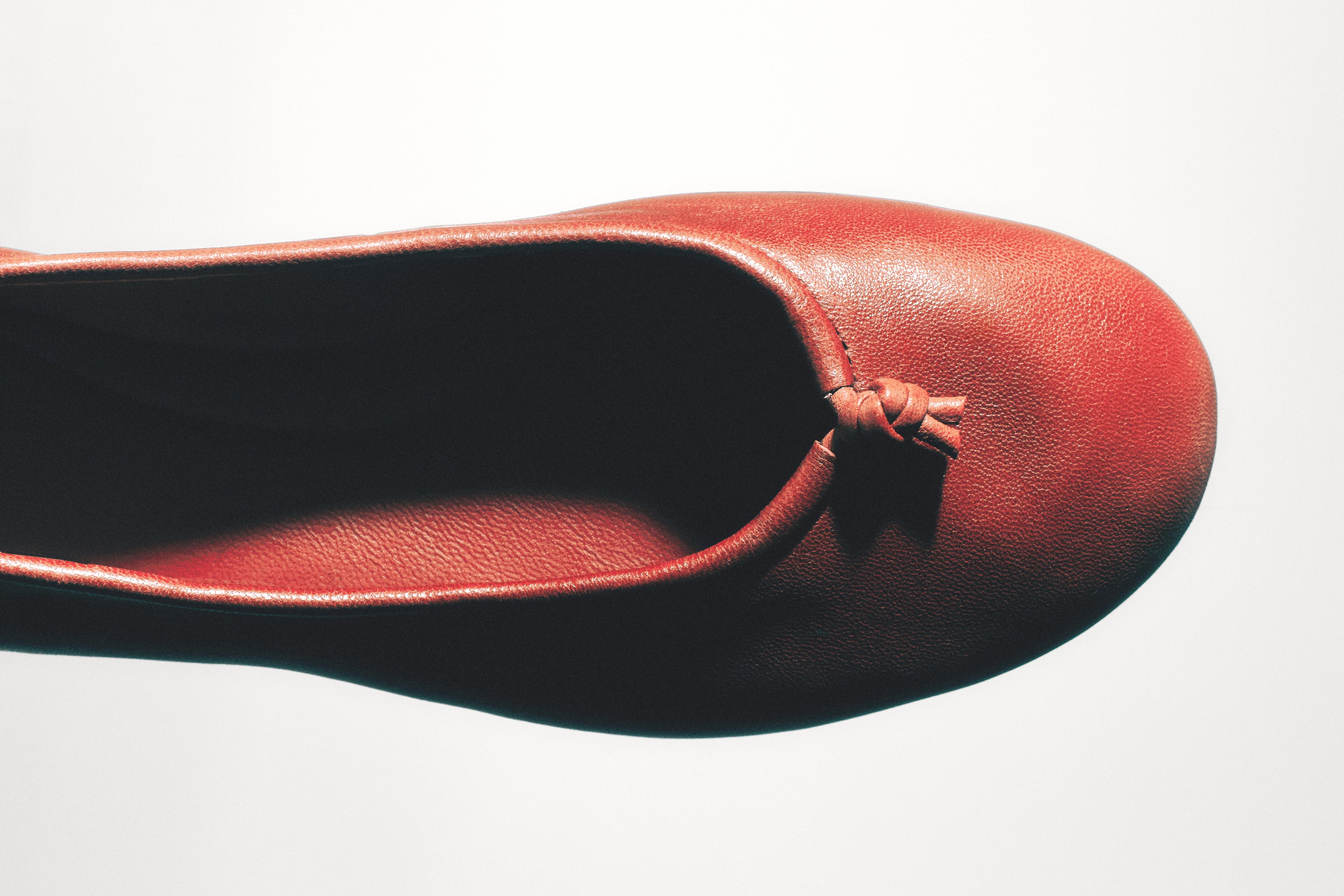 Halve foto van een rode ballerina met een decoratieve knoop aan de bovenkant.