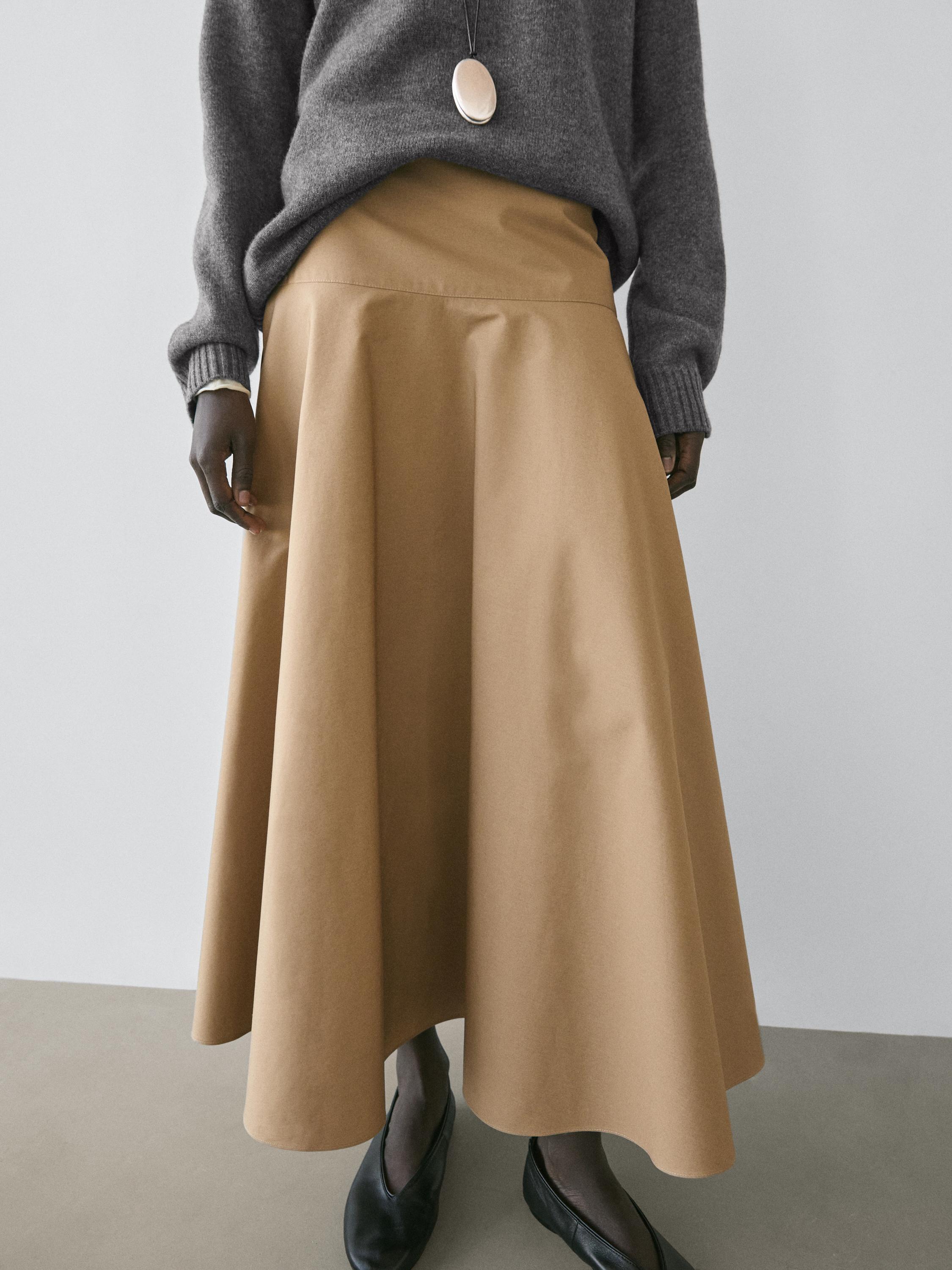 Σετ φούστα μίντι σε χρώμα camel με ζώνη και βολάν, γκρι πουλόβερ και μαύρα παπούτσια.