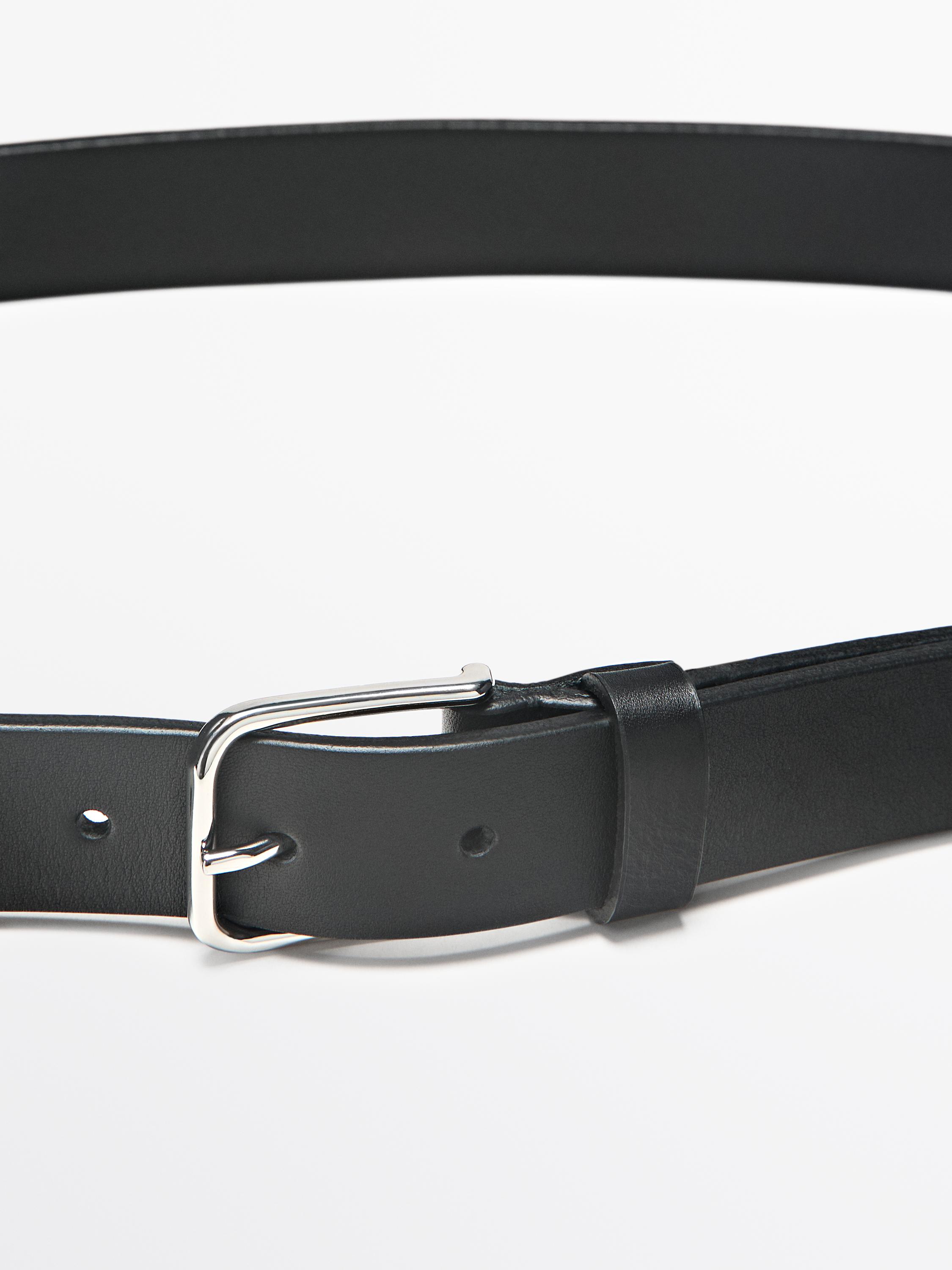 Nærbilde av svart belte med sølvfarget metallspenne og synlige hull.