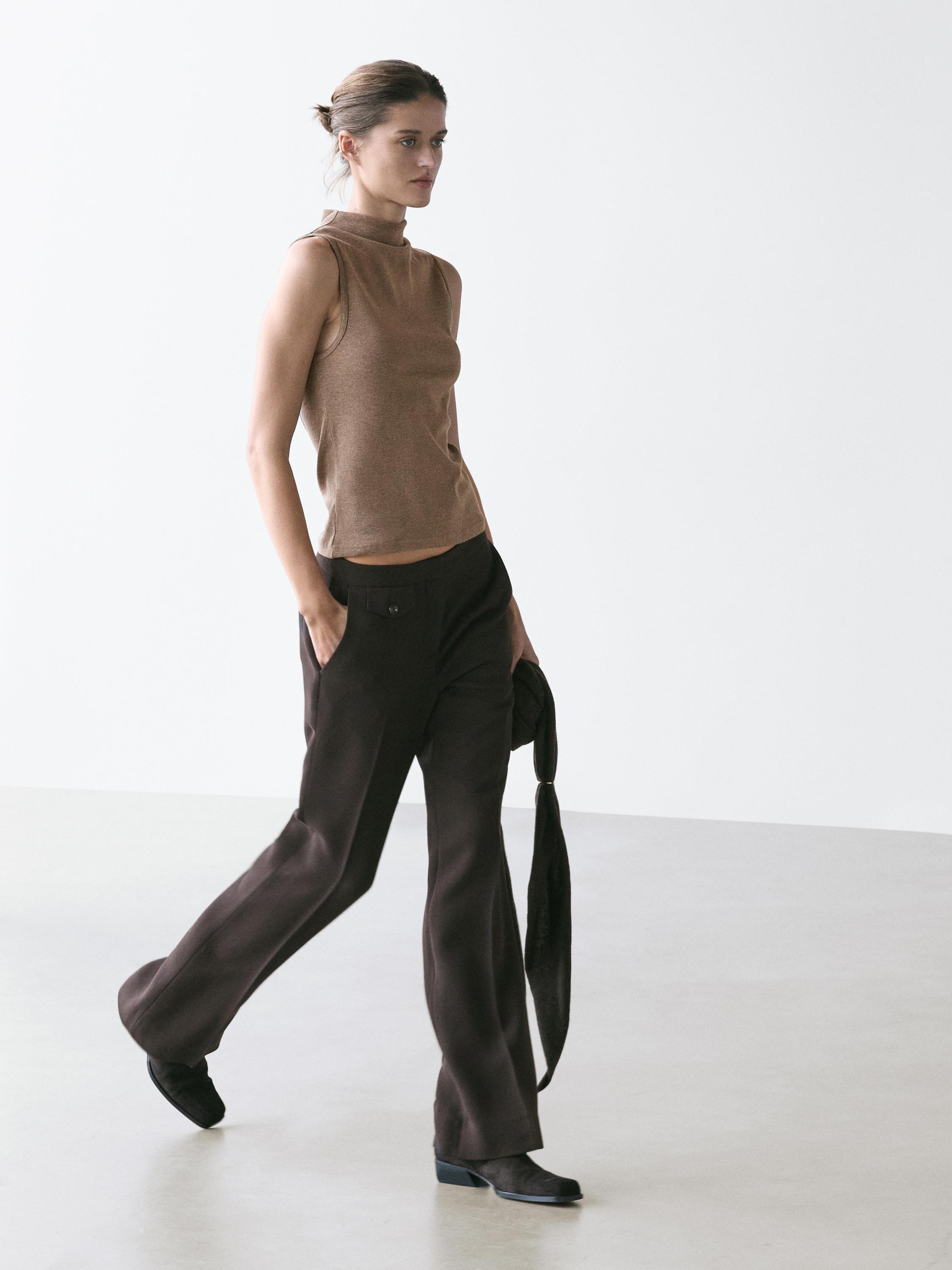 Conjunto de top sin mangas visón con cuello chimenea y pantalones oscuros de pierna ancha con bolsillos laterales.