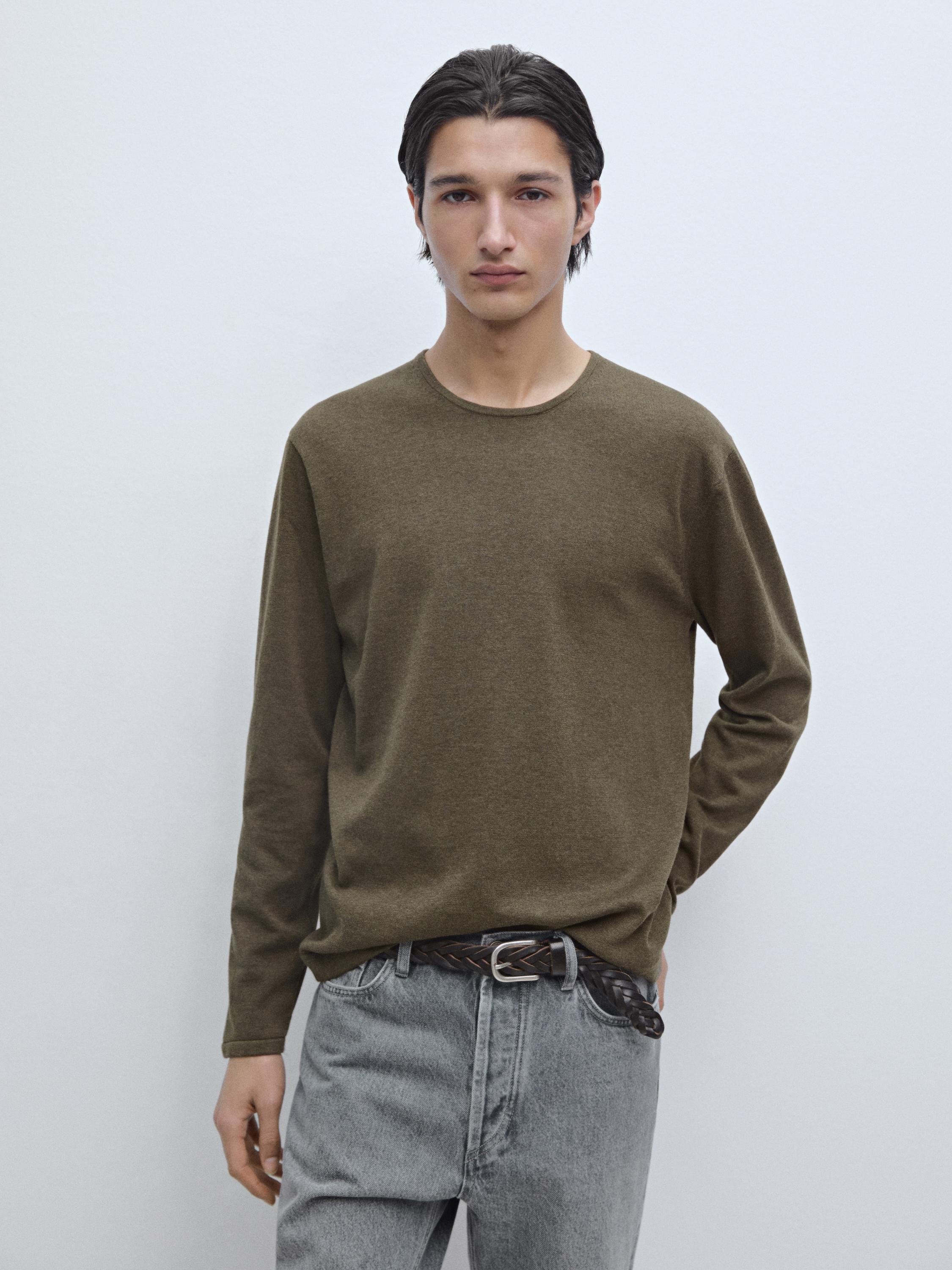 Setelan jersey hijau rajutan halus dengan kerah bundar dan jeans abu-abu.