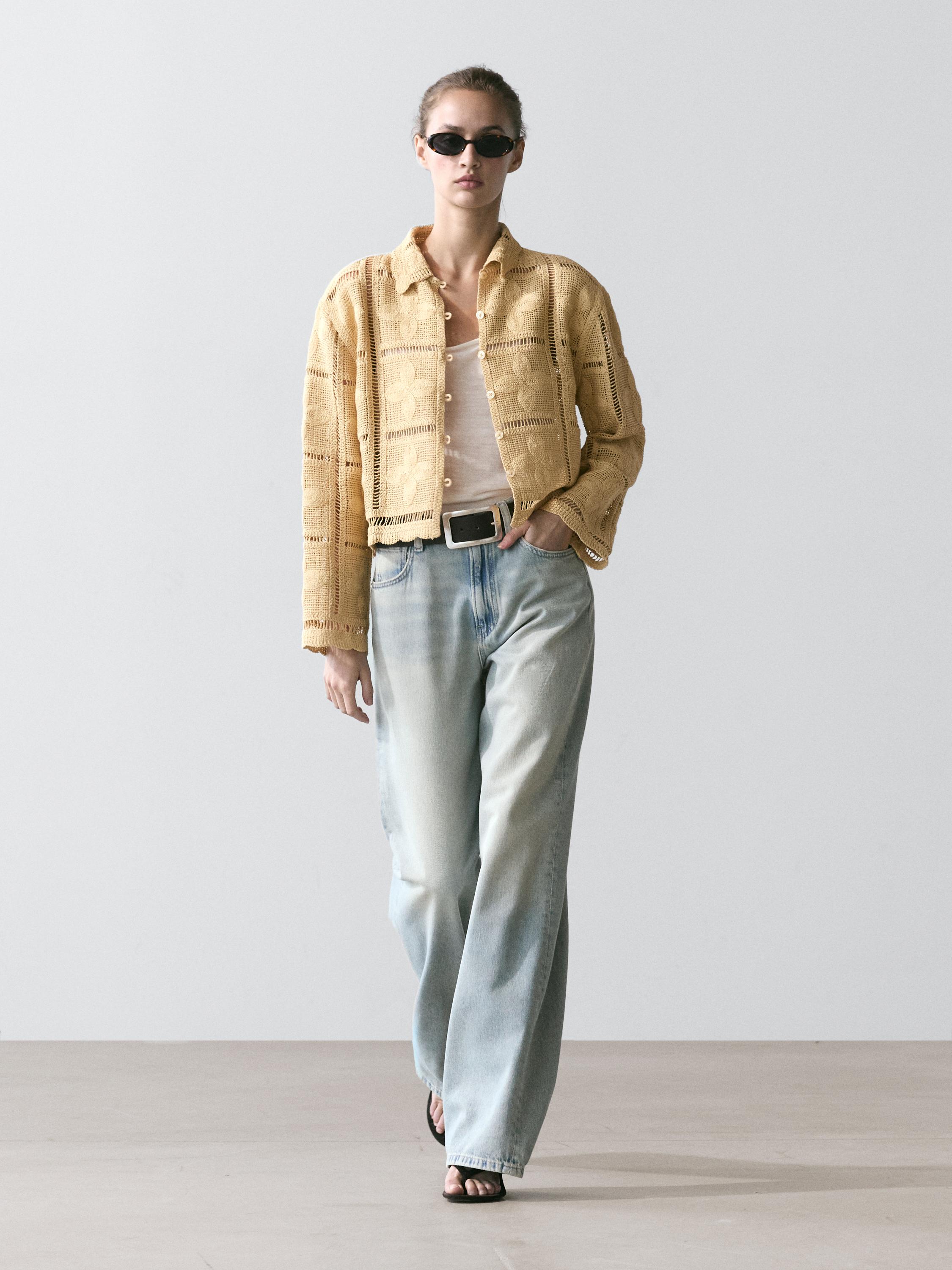 Vanillekleurige gebreide open-knit cardigan met knopen, wit T-shirt, lichtblauwe wijde jeans en zwarte sandalen.