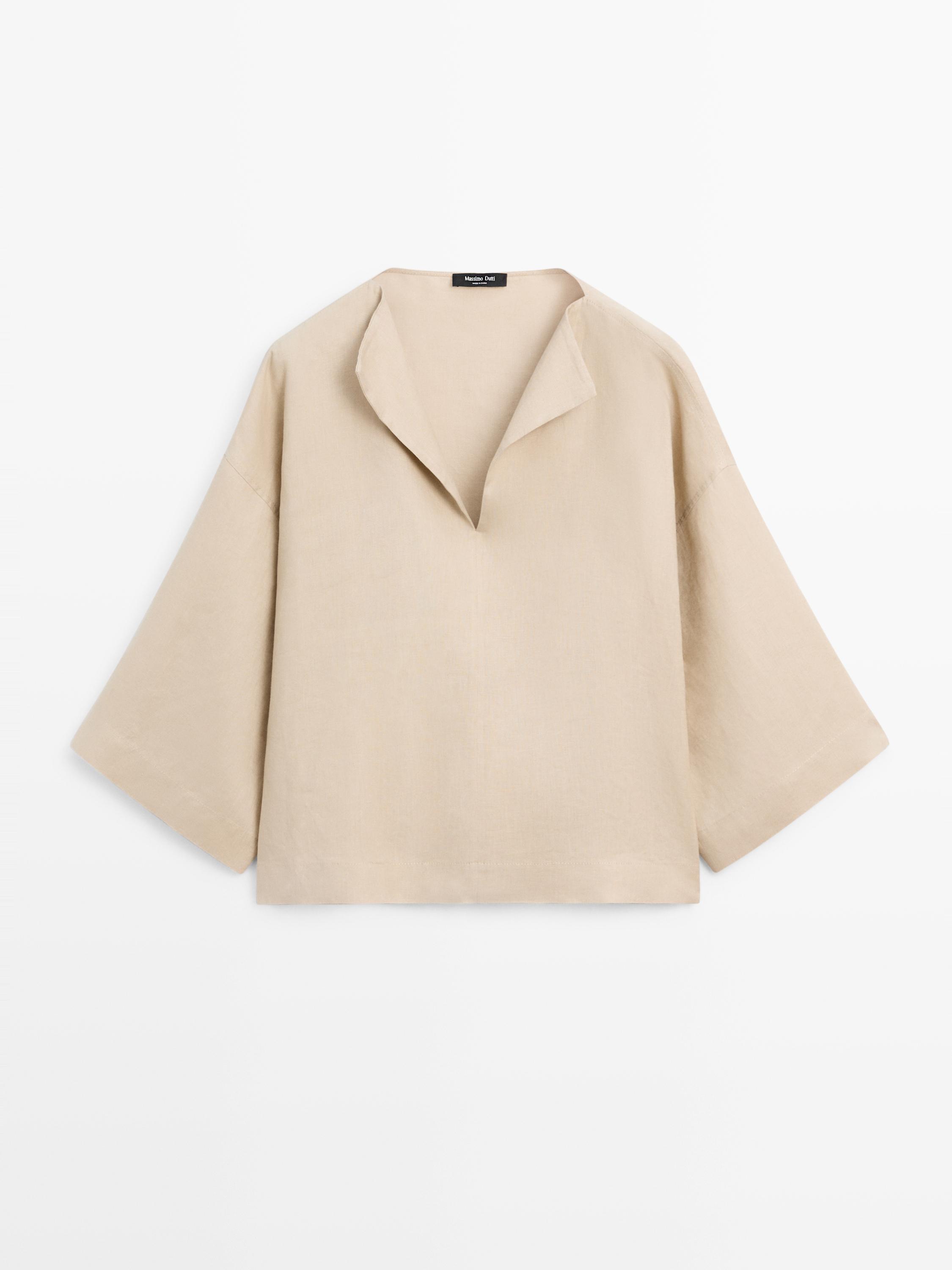 Front view of a sand-colored blouse with an open neck and wide long sleeves.