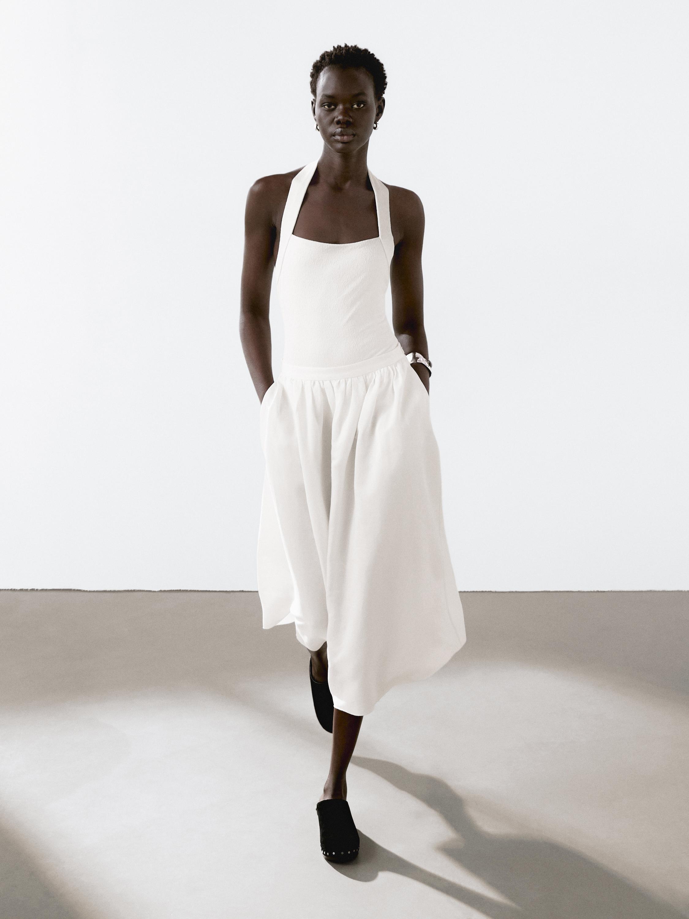 طقم فستان أبيض بحمالات وتنورة واسعة، وحذاء أسود.