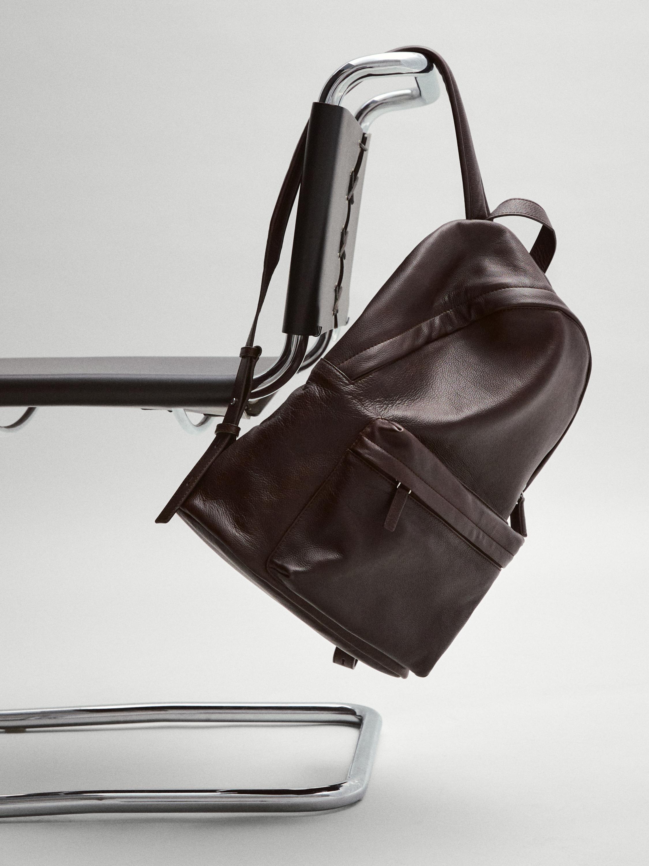 Vista lateral de mochila castanha com bolso frontal com fecho éclair e pega superior.