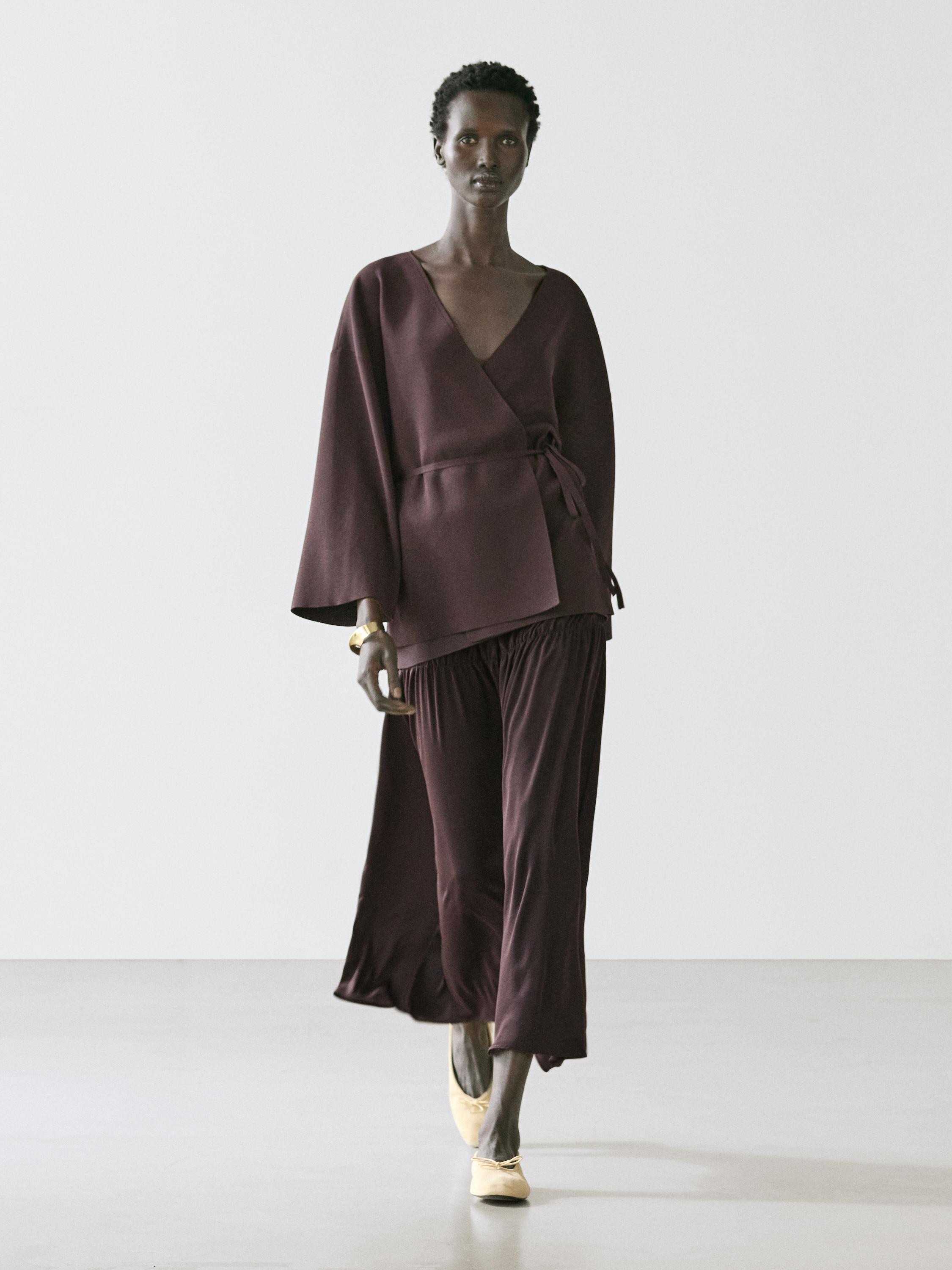 Luźny brązowy komplet kimono z paskiem i dopasowanymi spodniami, beżowe buty.