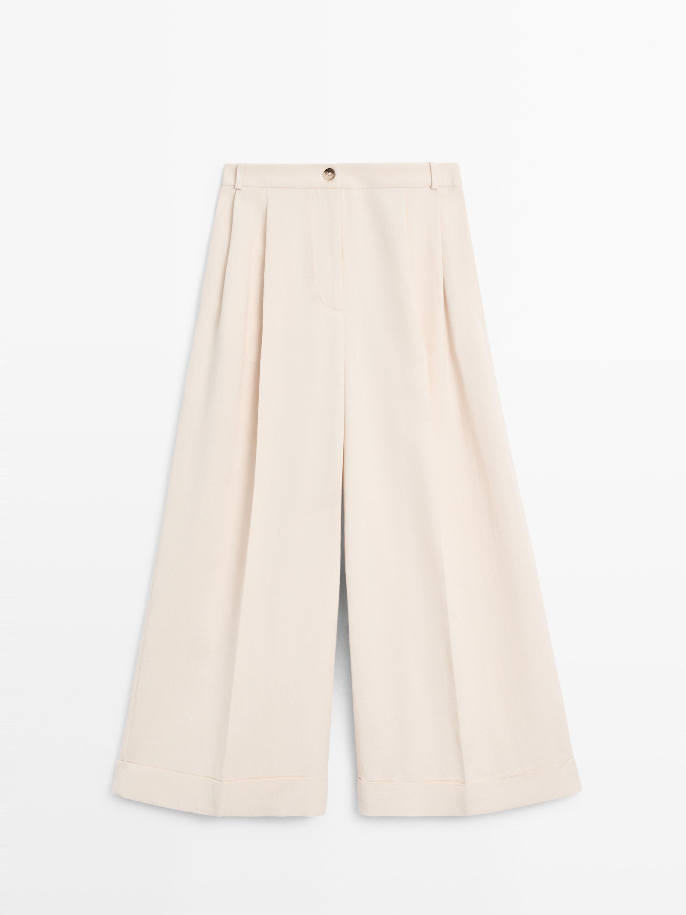 Front view of fluid ecru pants with a turned-up hem, front pleats, and button closure.