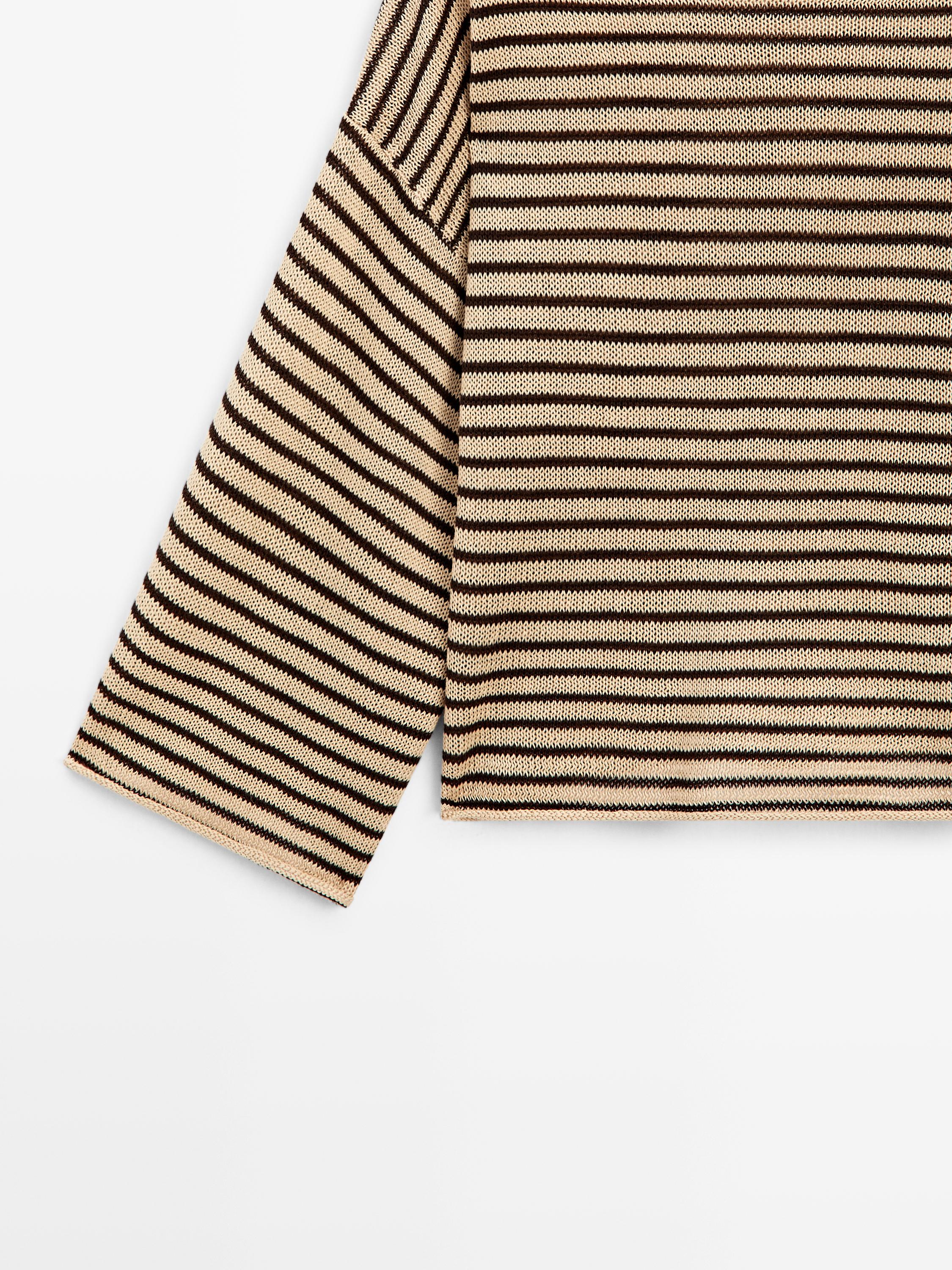 Detall de màniga i cos de jersei tricot torrat amb ratlles horitzontals negres.