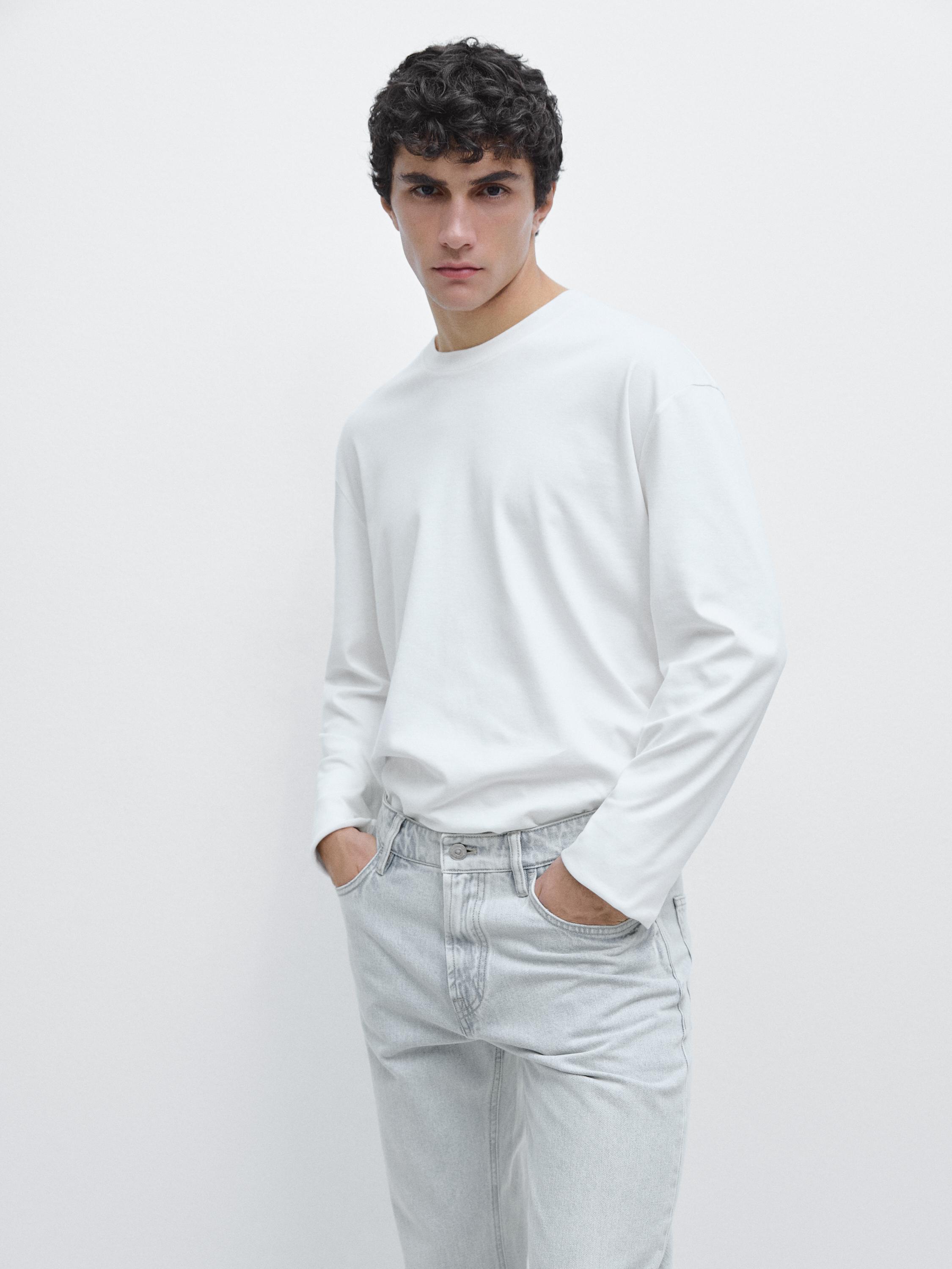 Komplet bluze të bardhë me mëngë të gjata dhe pantallona xhins të çelur me xhepa përpara.