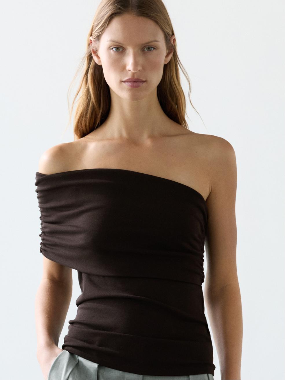 Plano médio de top castanho sem mangas, decote assimétrico drapeado, justo ao corpo.