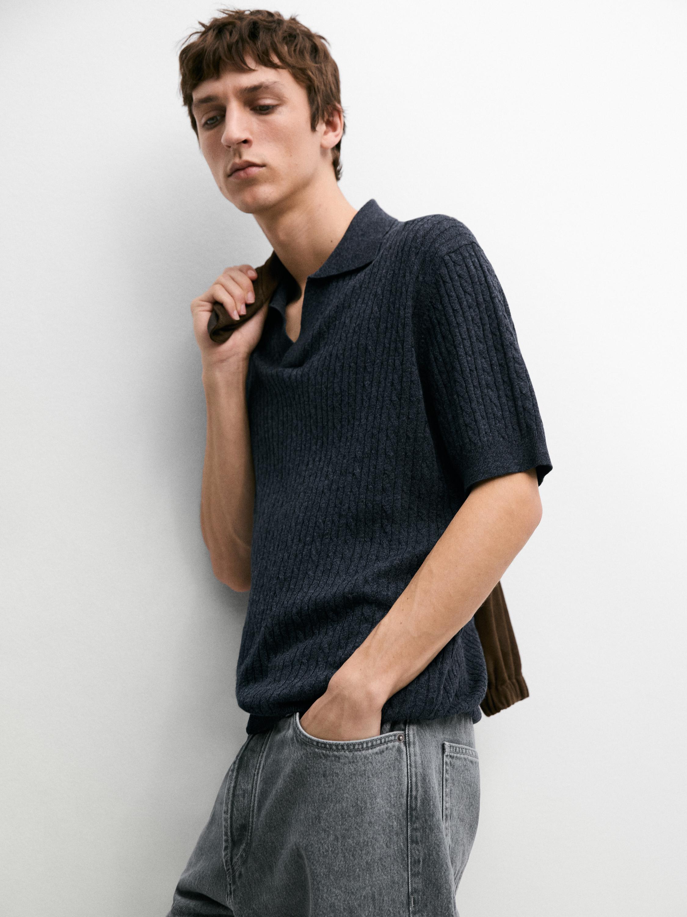 Plano medio de polo azul marino con detalle trenzado y mangas cortas, combinado con pantalón gris y bolsillos laterales.