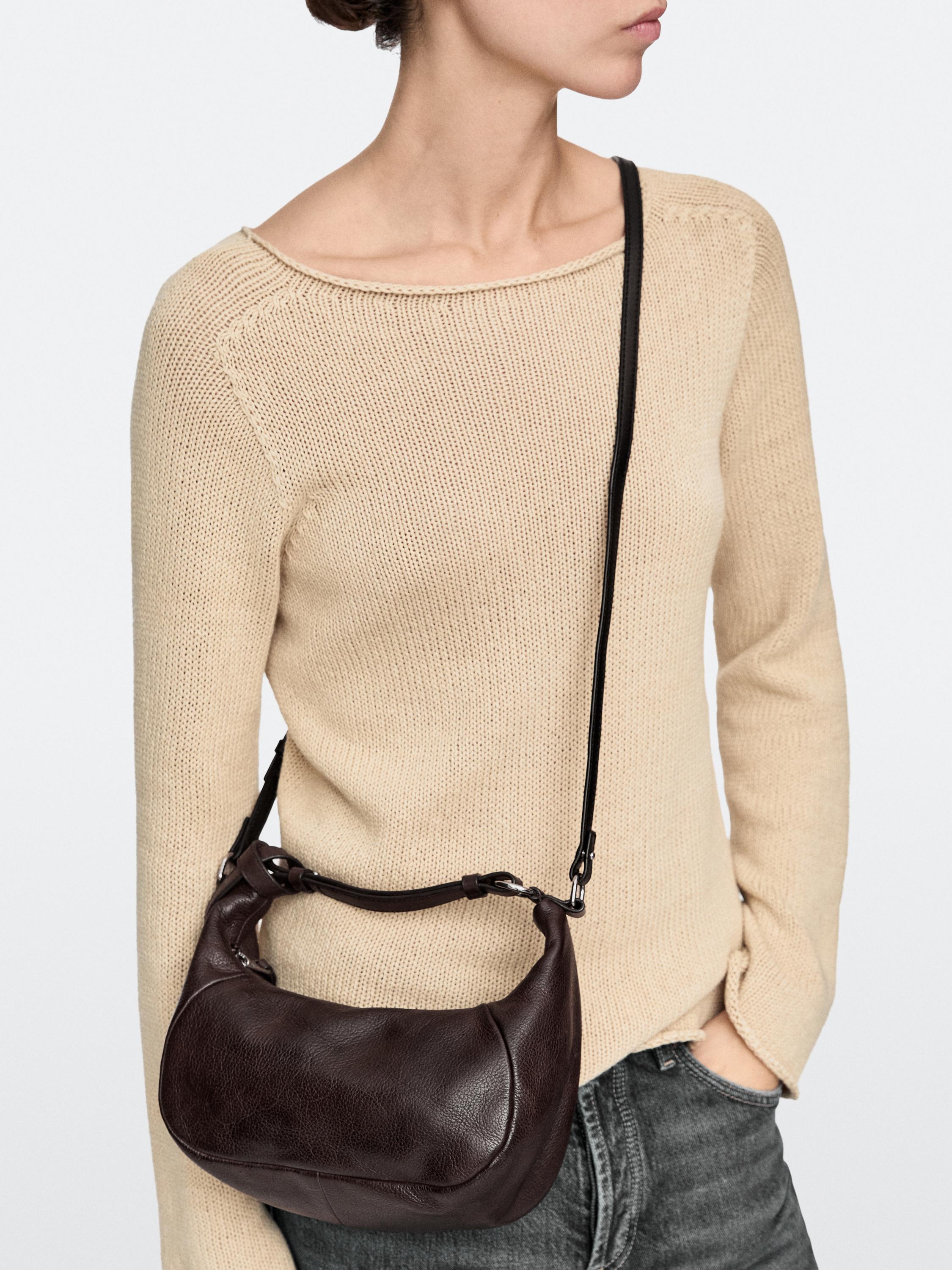 Ayarlanabilir askılı kahverengi çanta seti ve beli görünen bej örgü kazak.