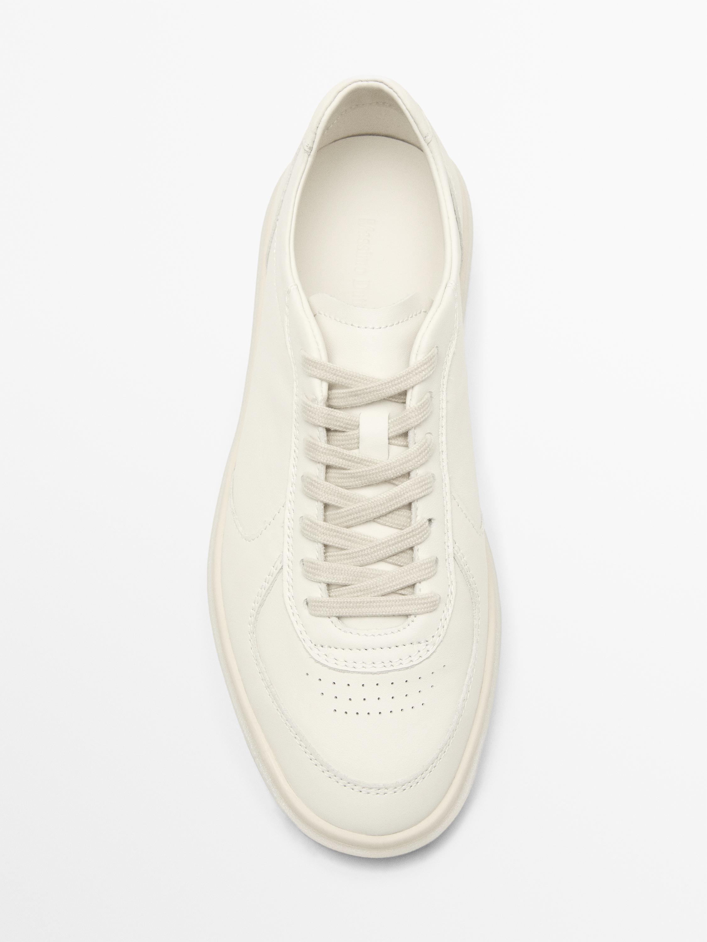 Vue de dessus d'une basket blanche avec des lacets et des perforations sur la pointe.