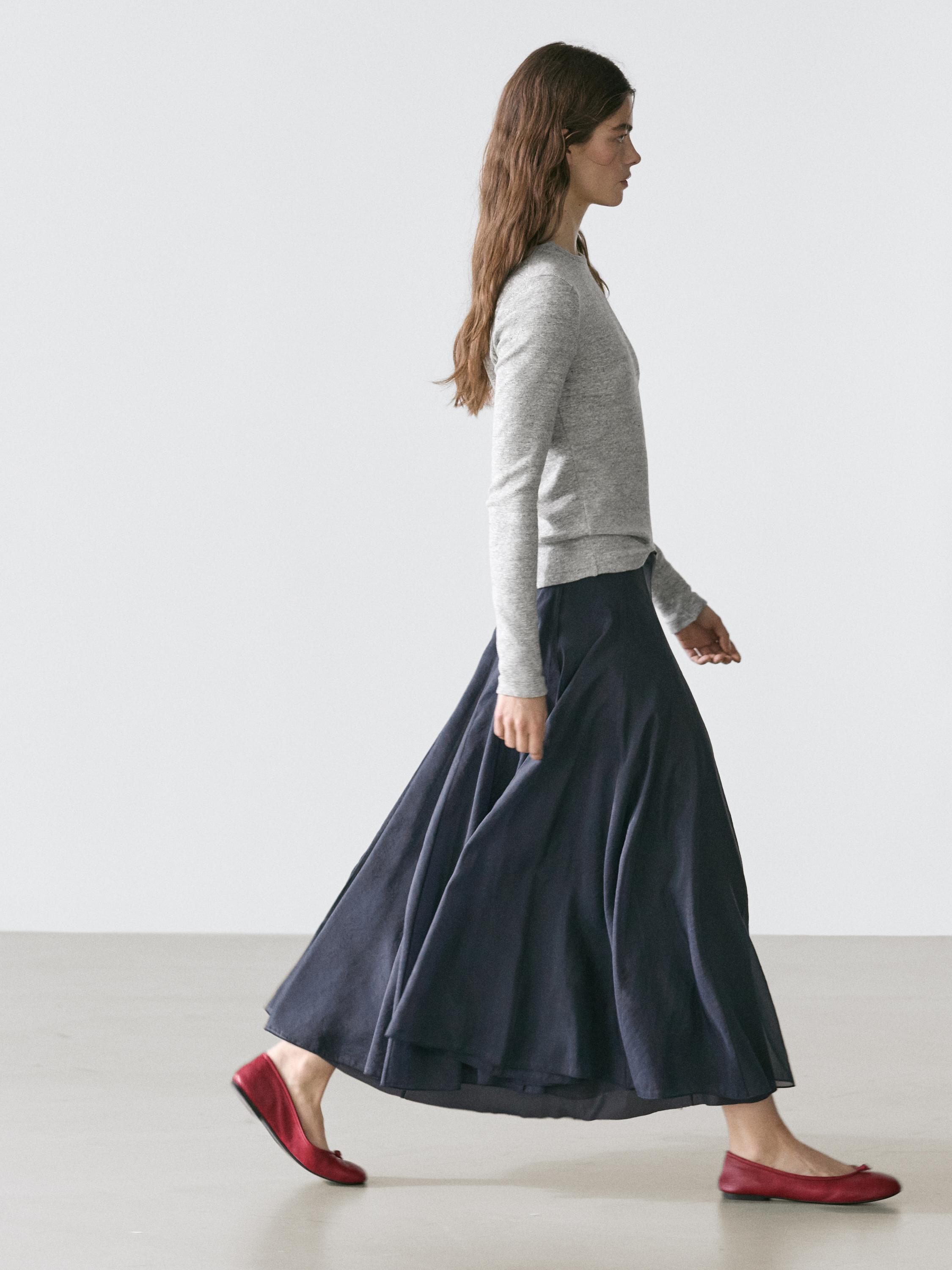 Conjunt de faldilla midi blau fosc amb plecs i jersei gris de màniga llarga.