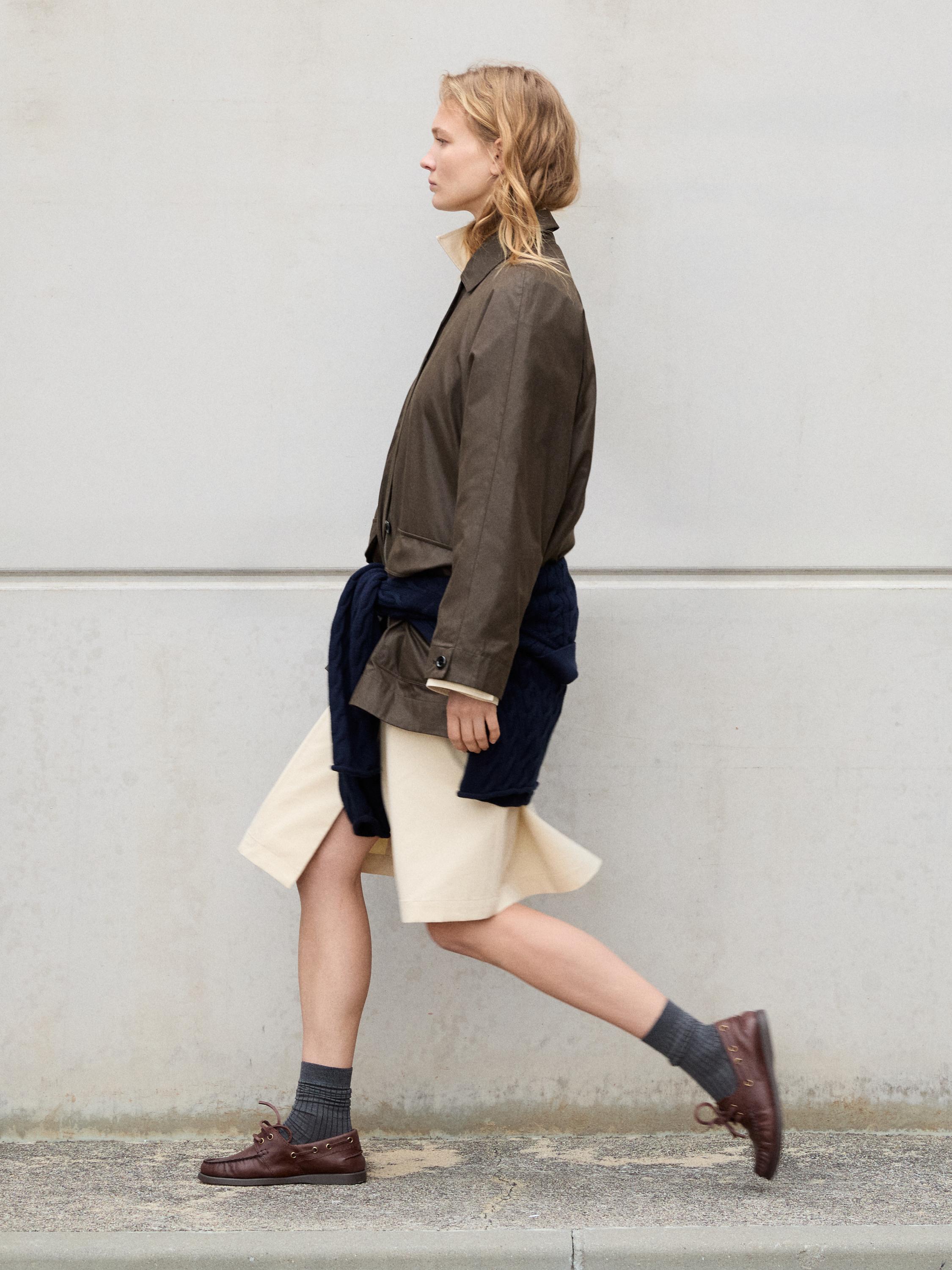 Kahverengi ceket, bej etek, bele bağlanmış mavi kazak, gri çoraplar ve kahverengi makosen ayakkabılar.