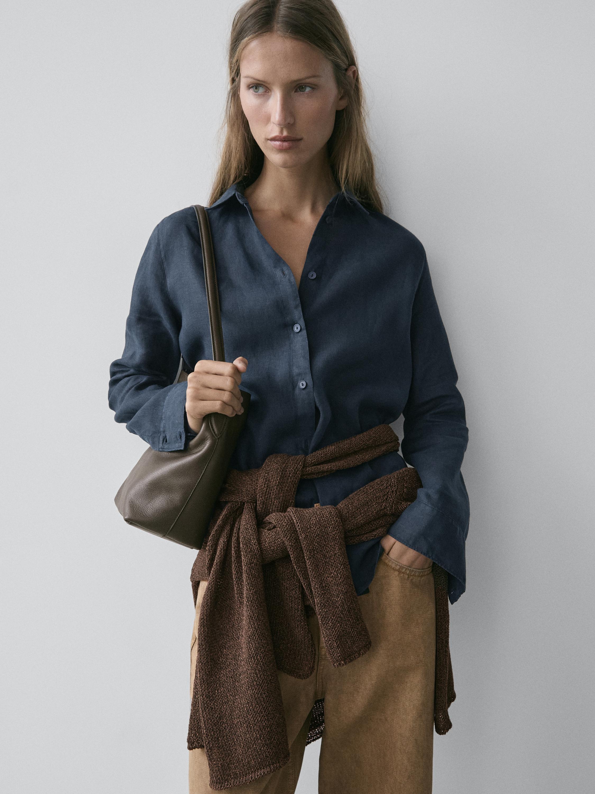 Navy blue button-down shirt and beige pants set. Brown sweater tied at the waist and brown shoulder bag.