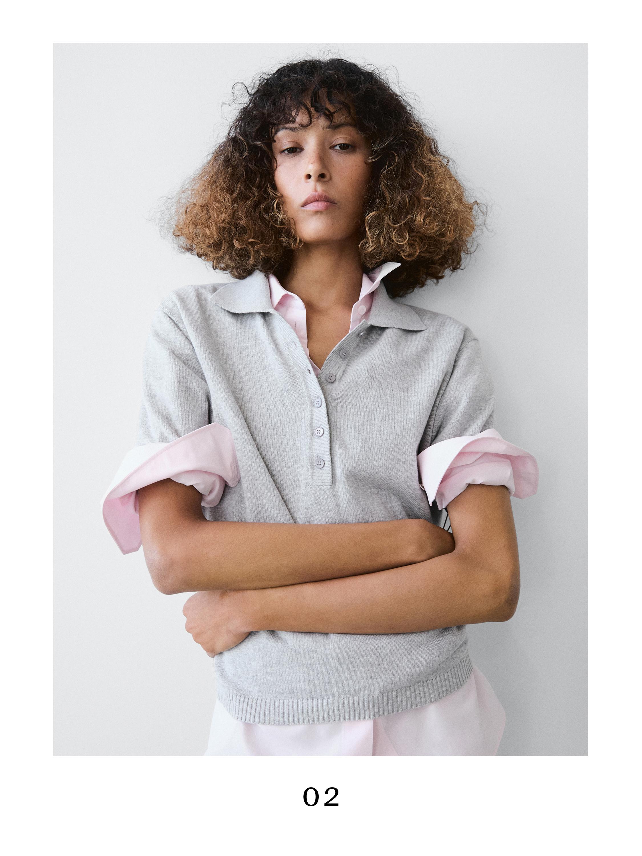 Medium shot of a light gray polo shirt with a collar and placket, over a pink shirt with folded sleeves.