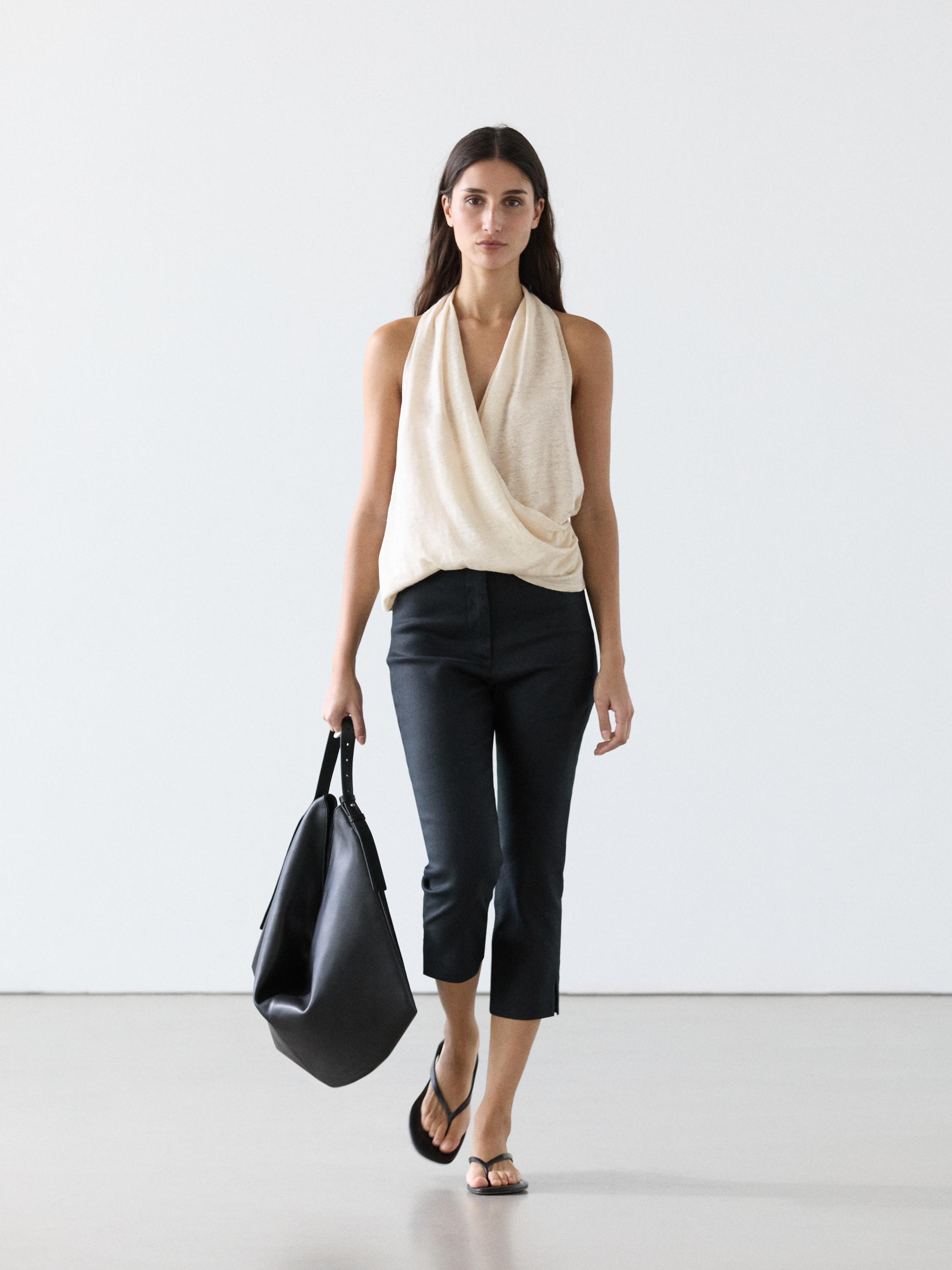 Conjunto de top beige sin mangas cruzado con detalle drapeado y pantalones capri negros.