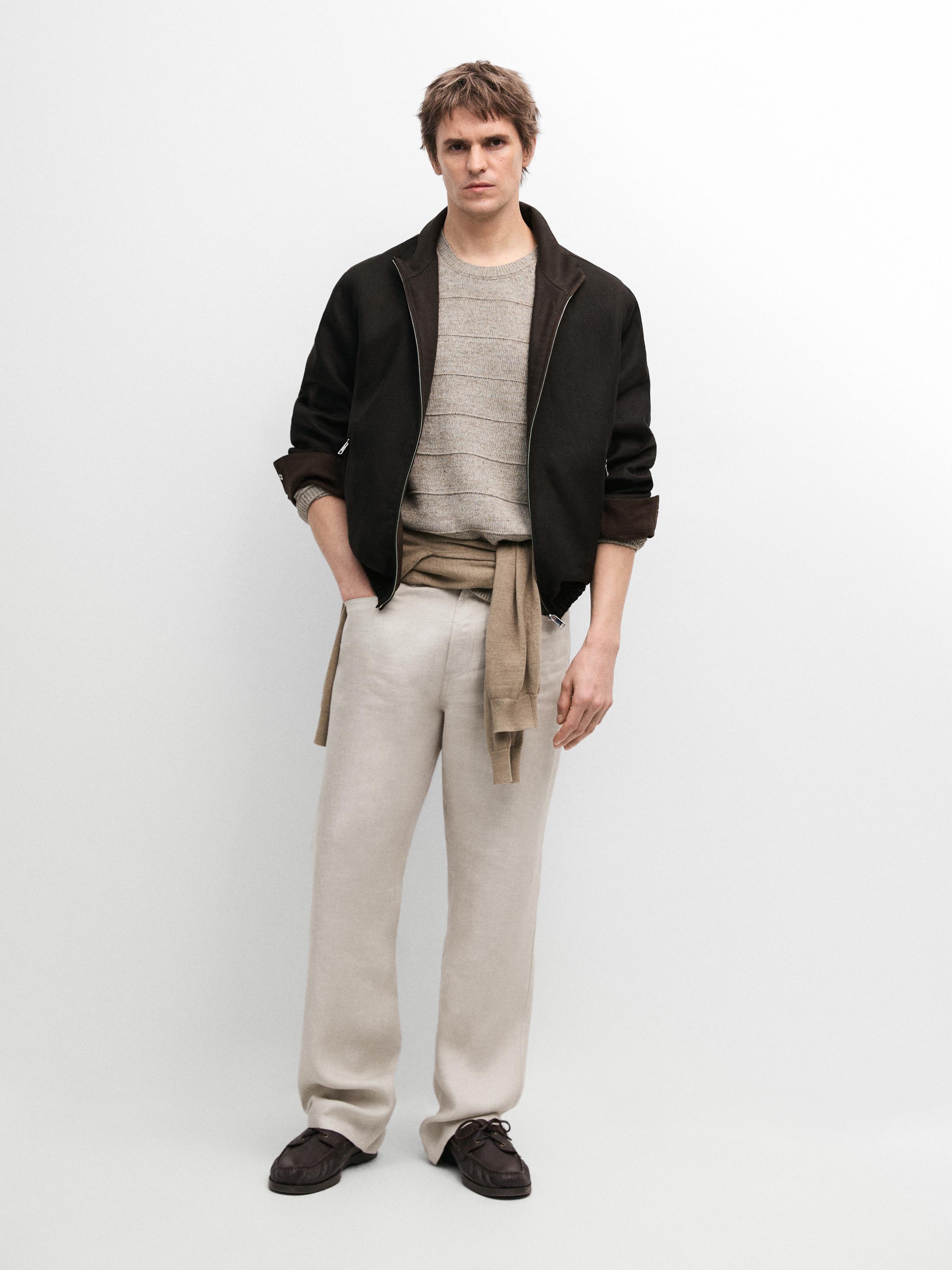 Set aus schwarzer Reißverschlussjacke, beigefarbenem Ringelpullover, heller Hose und dunklen Schuhen.