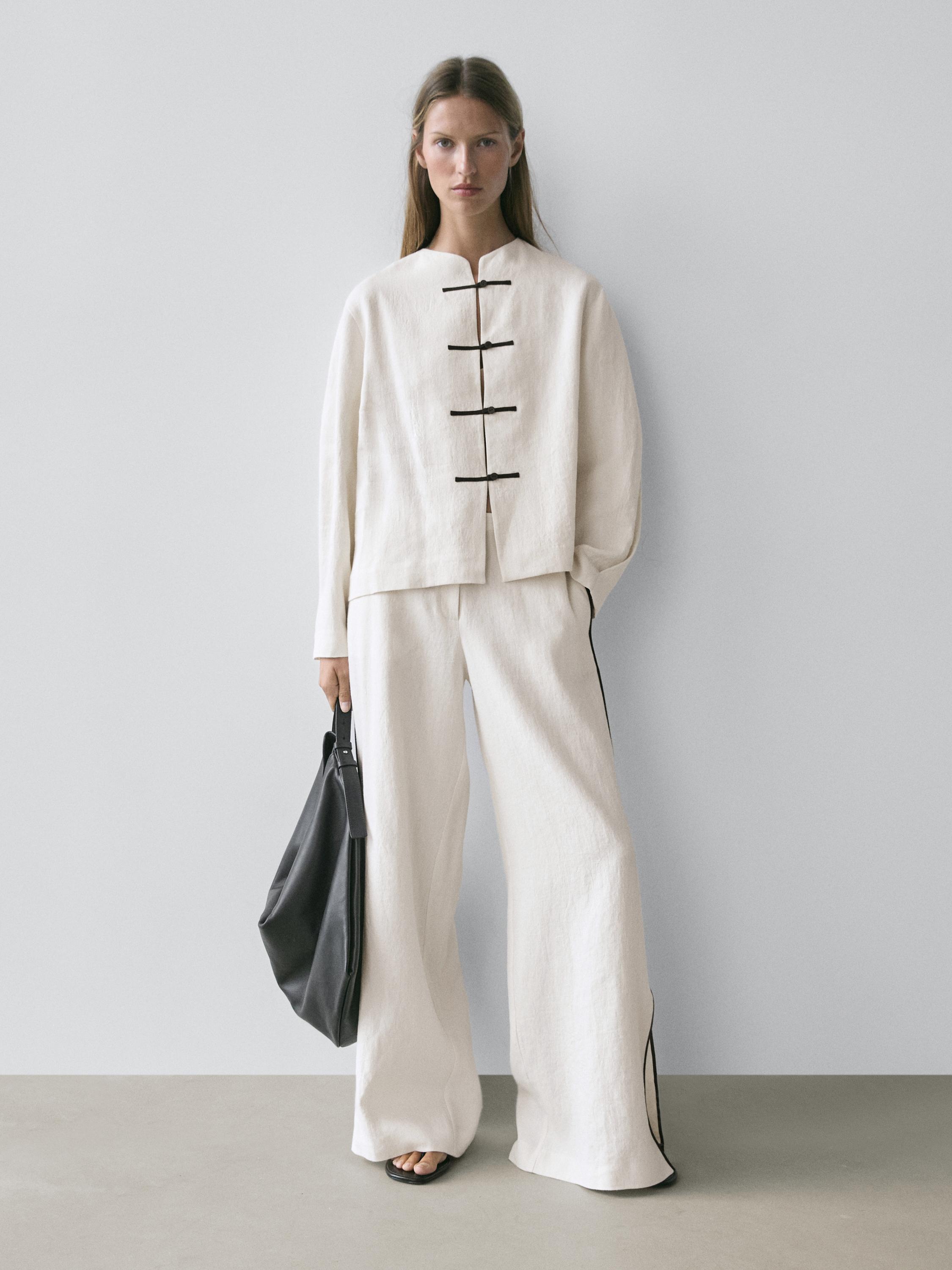 Conjunto de chaqueta beige con cierre de lazos negros y pantalones anchos a juego.