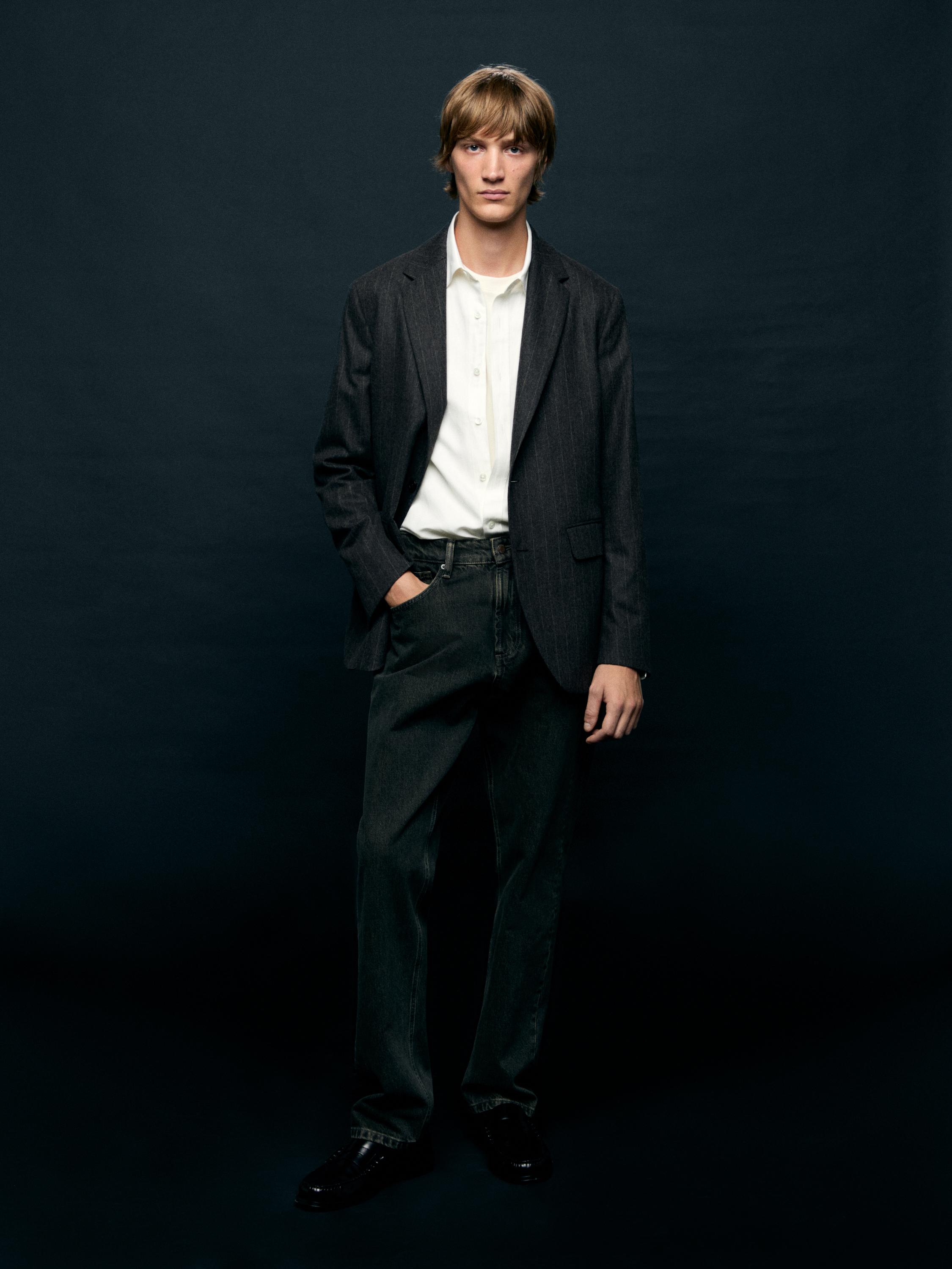 Комплект из черного пиджака, белой рубашки и темных брюк с боковыми карманами.