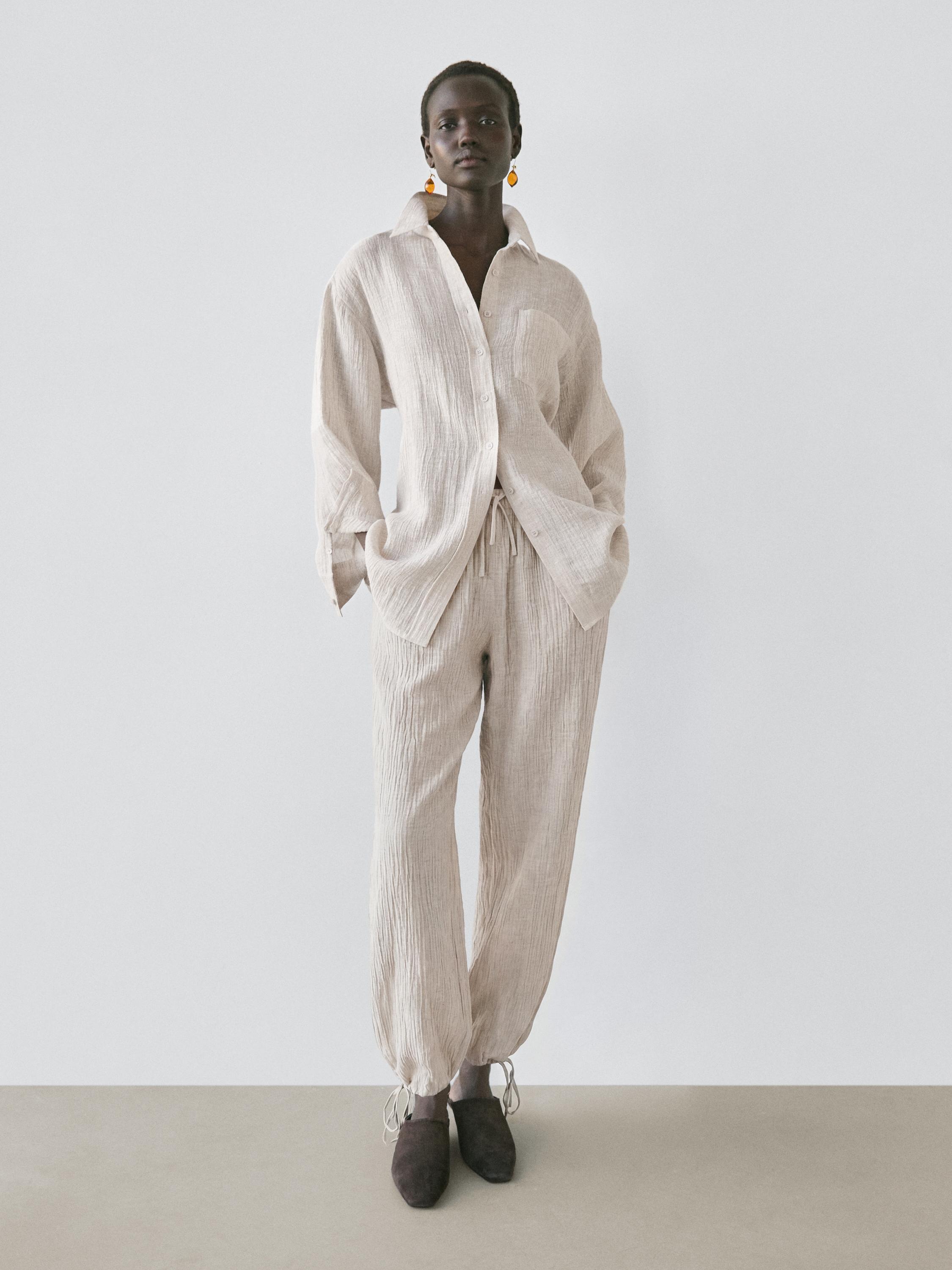 Conjunto de camisa beige de manga larga con botones y pantalones a juego con cordones en los tobillos.