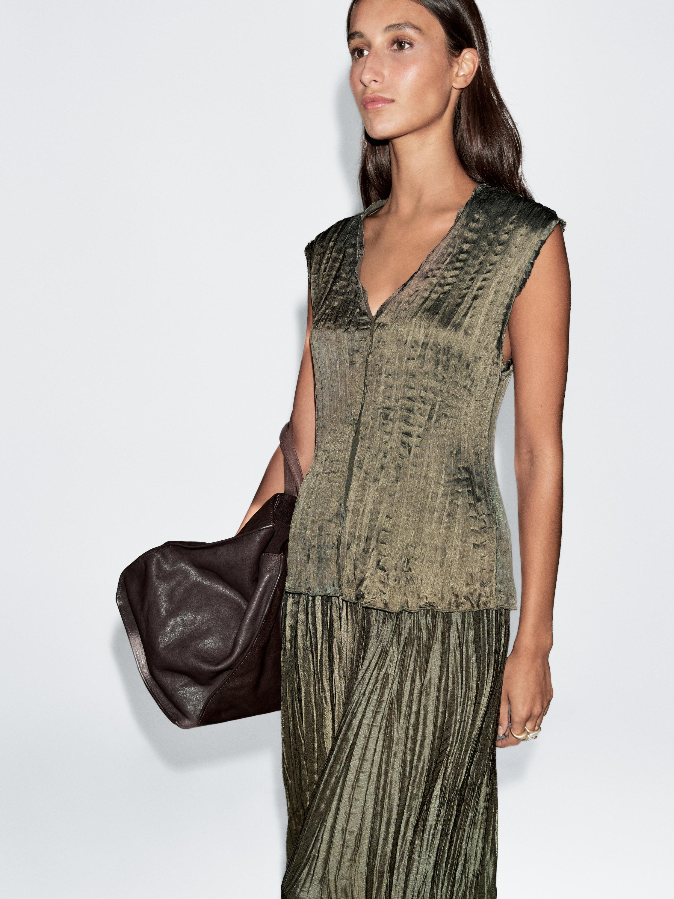 لقطة متوسطة لبلوزة بدون أكمام باللون الزيتوني الفاتح مع نسيج مجعد وياقة على شكل حرف V.