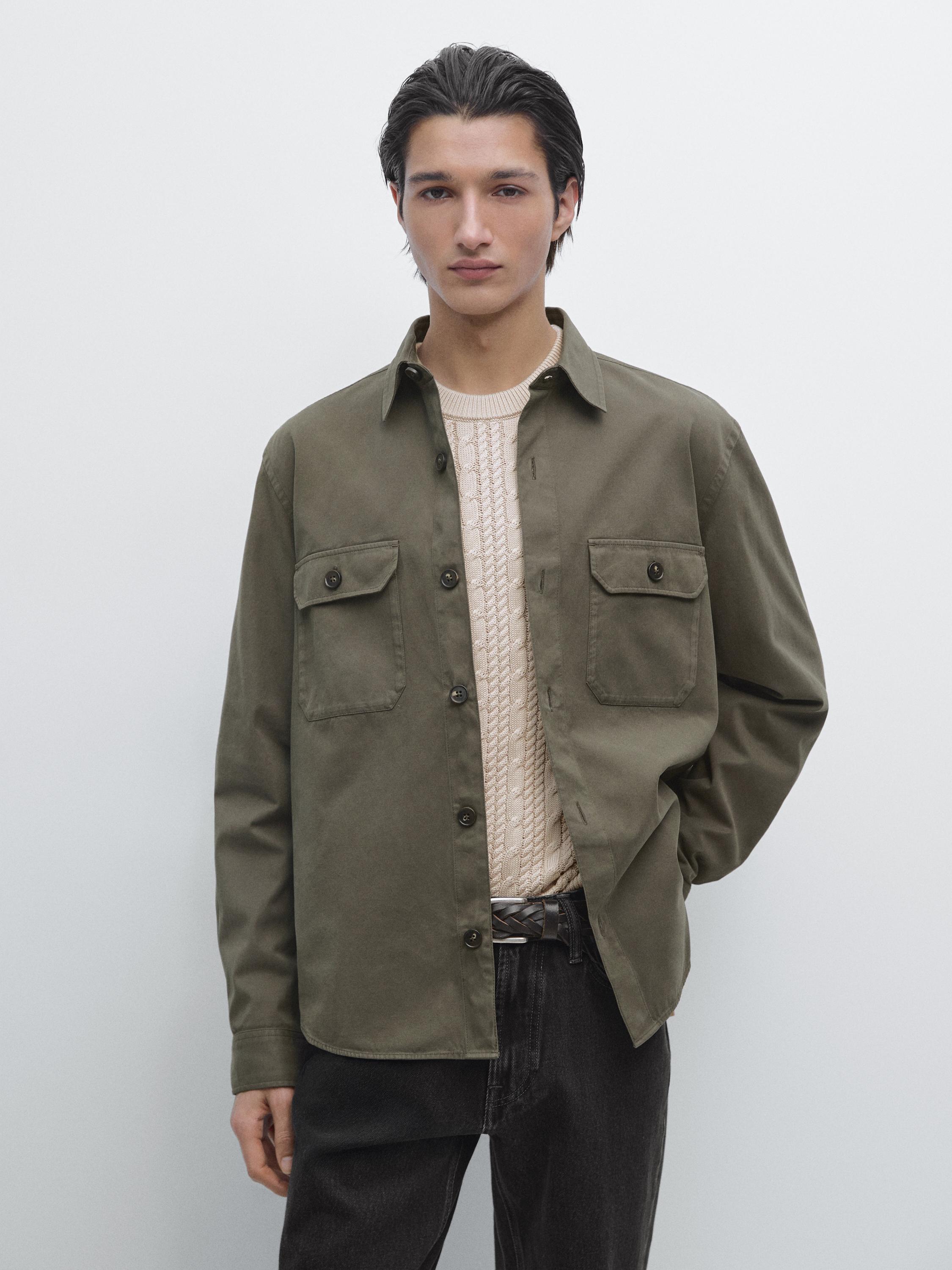 Green overshirt set with front pockets and buttons, knitted beige sweater, and dark pants.