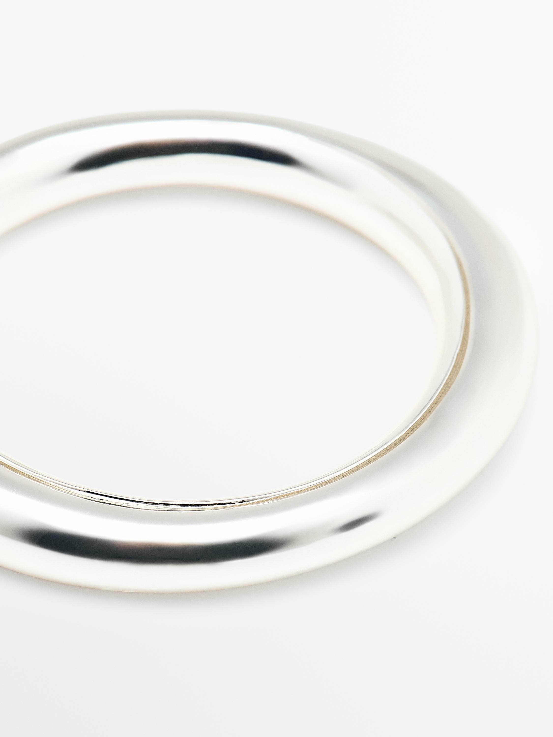 "Close-up van een stijve, zilverkleurige armband met een glad ontwerp en een glanzende afwerking."