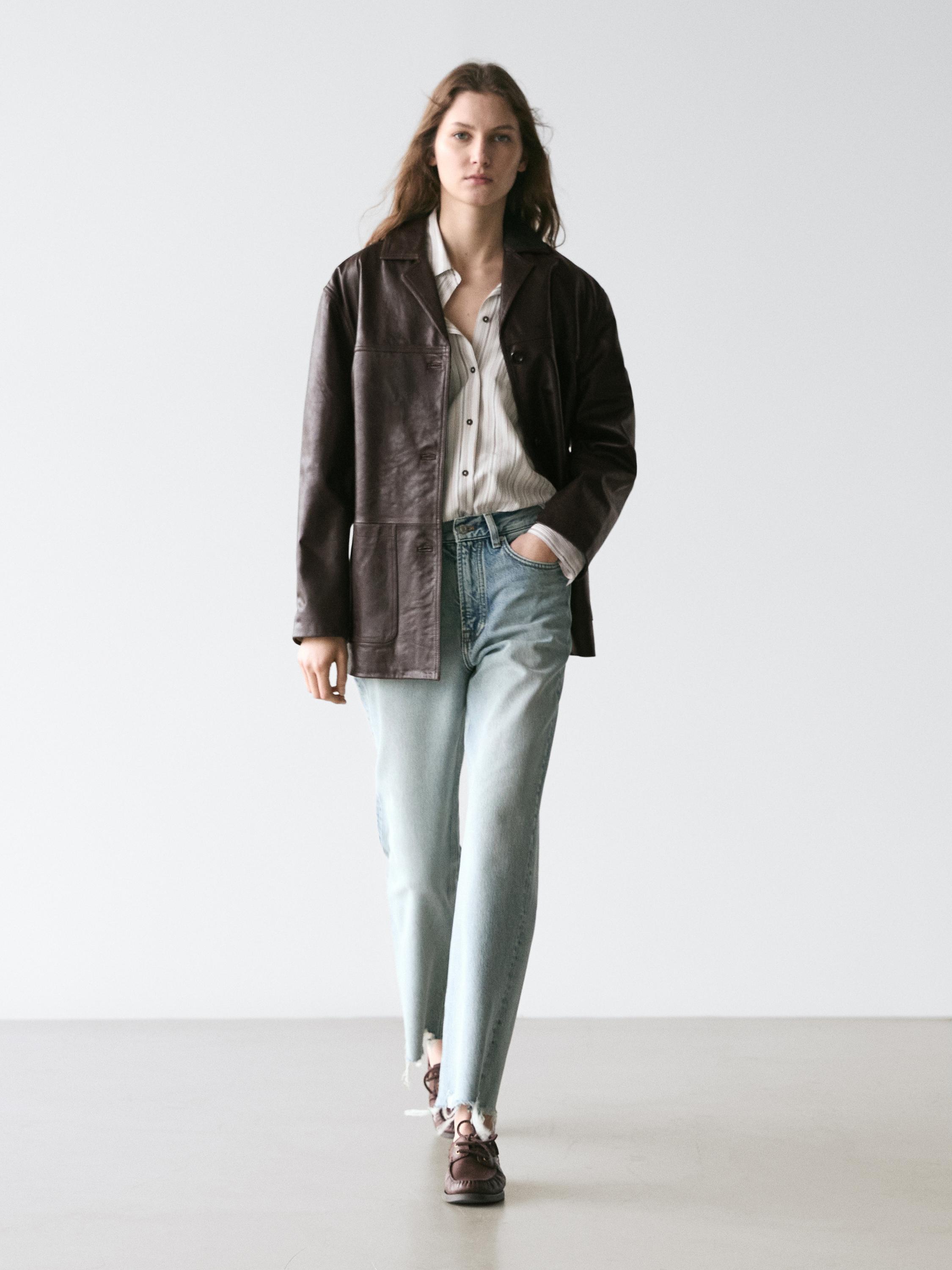 Ensemble composé d'une veste marron, d'une chemise blanche à rayures, d'un jean bleu clair taille haute et de chaussures marron.