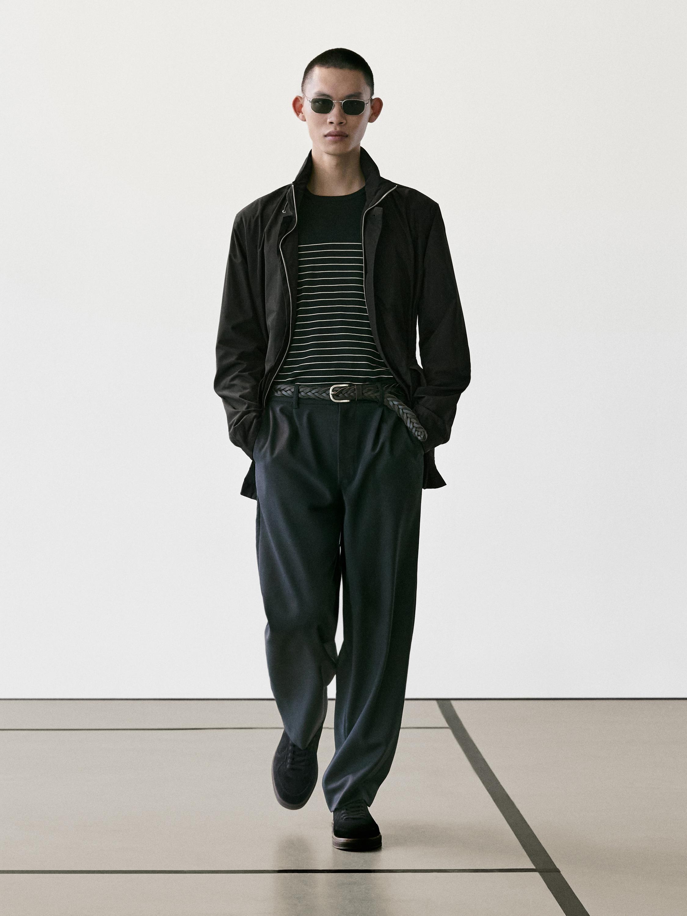 طقم يتكون من سترة سوداء، وقميص مخطط أفقيًا، وبنطلون داكن مع حزام مضفر، وحذاء أسود.