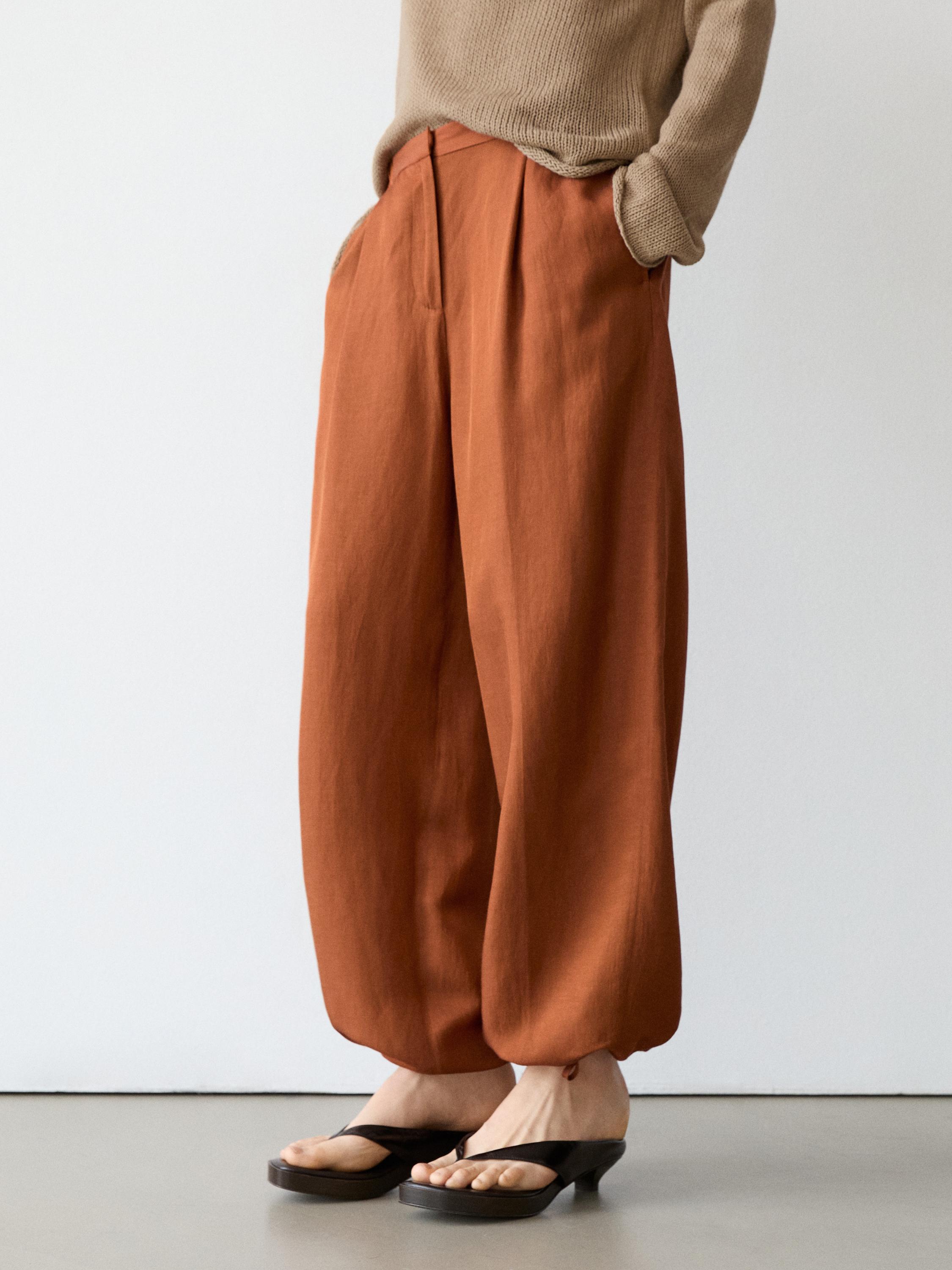 Półzbliżenie na pomarańczowe, zwiewne spodnie z wiązaniem przy kostkach i bocznymi kieszeniami.