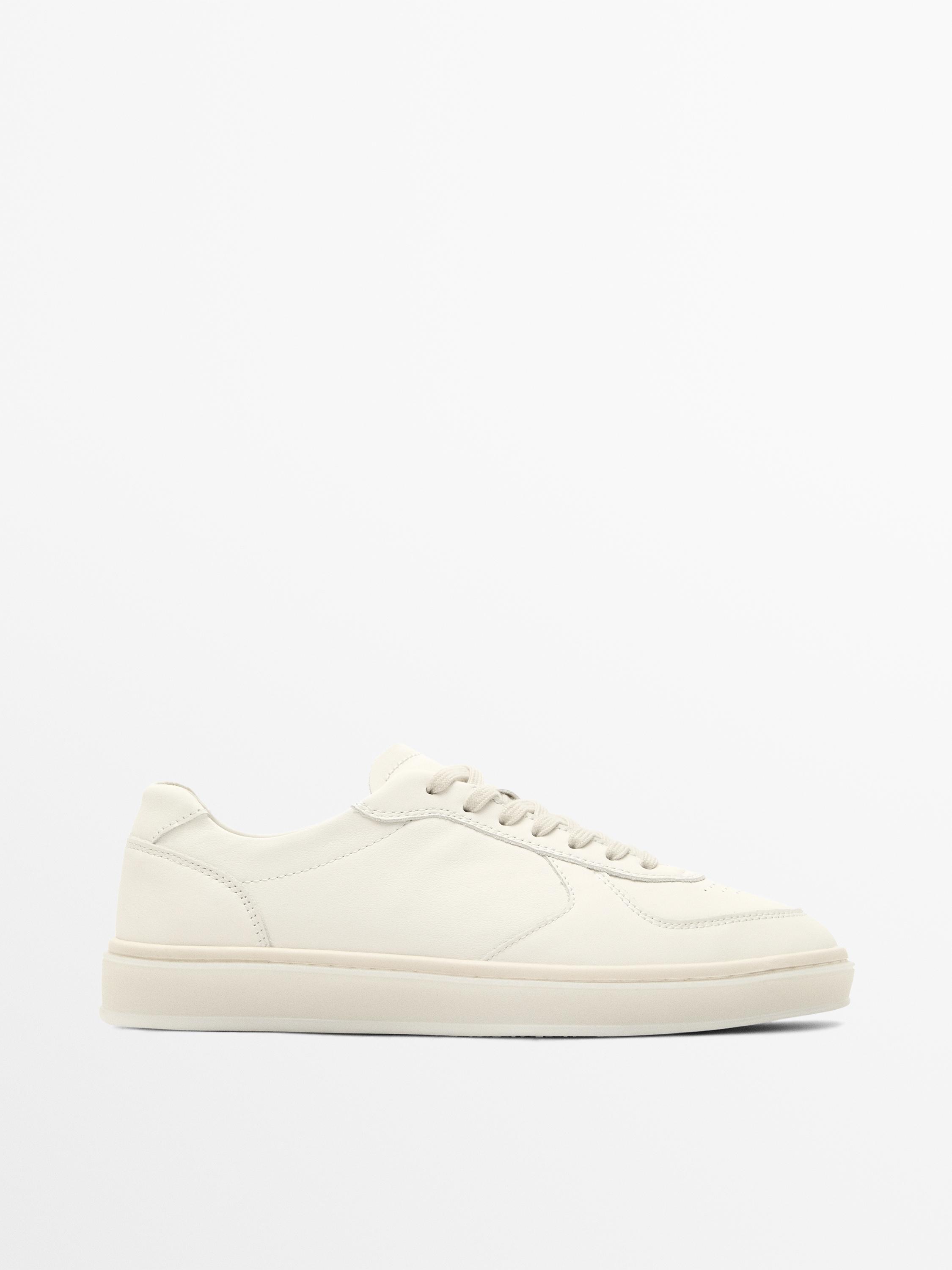 Vue latérale de baskets blanches avec lacets et semelle plate. Design minimaliste sans détails supplémentaires visibles.