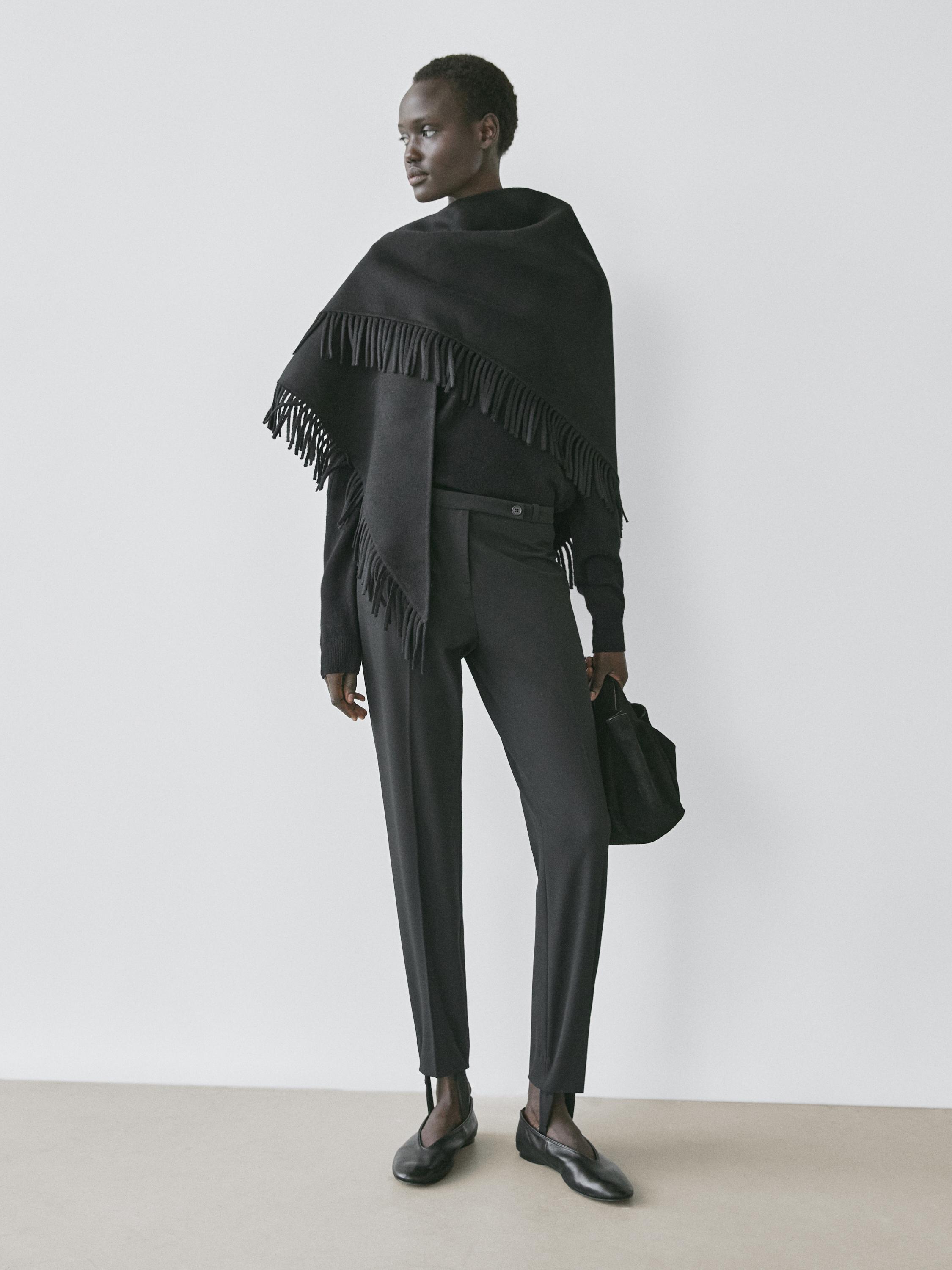 طقم بنطلون أسود بحافة مطاطية، وكنزة صوفية سوداء، وشال مع شراشيب.