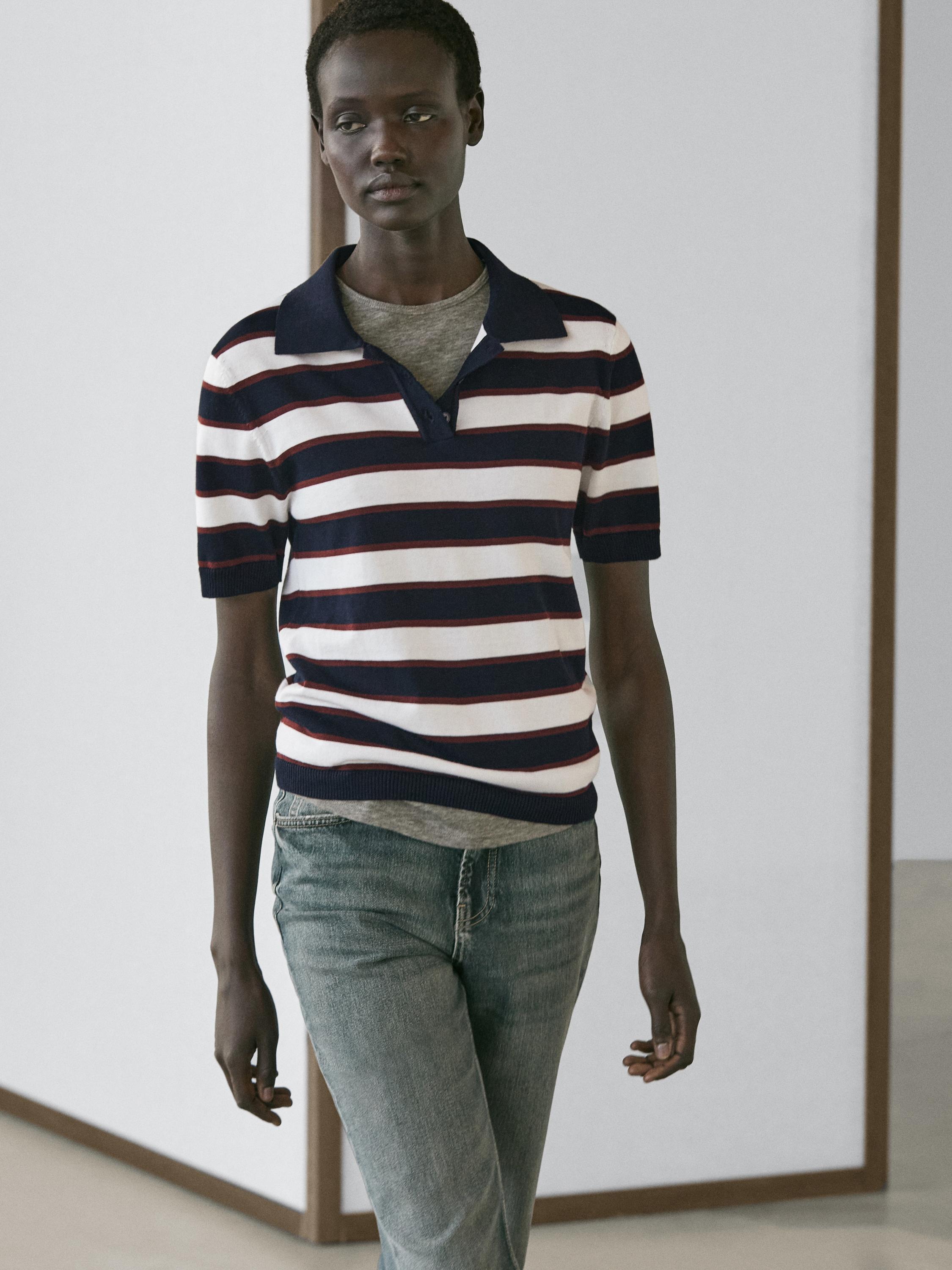 طقم بولو أزرق كحلي بخطوط بيضاء وحمراء، ياقة كلاسيكية وأكمام قصيرة، منسق مع جينز أزرق.