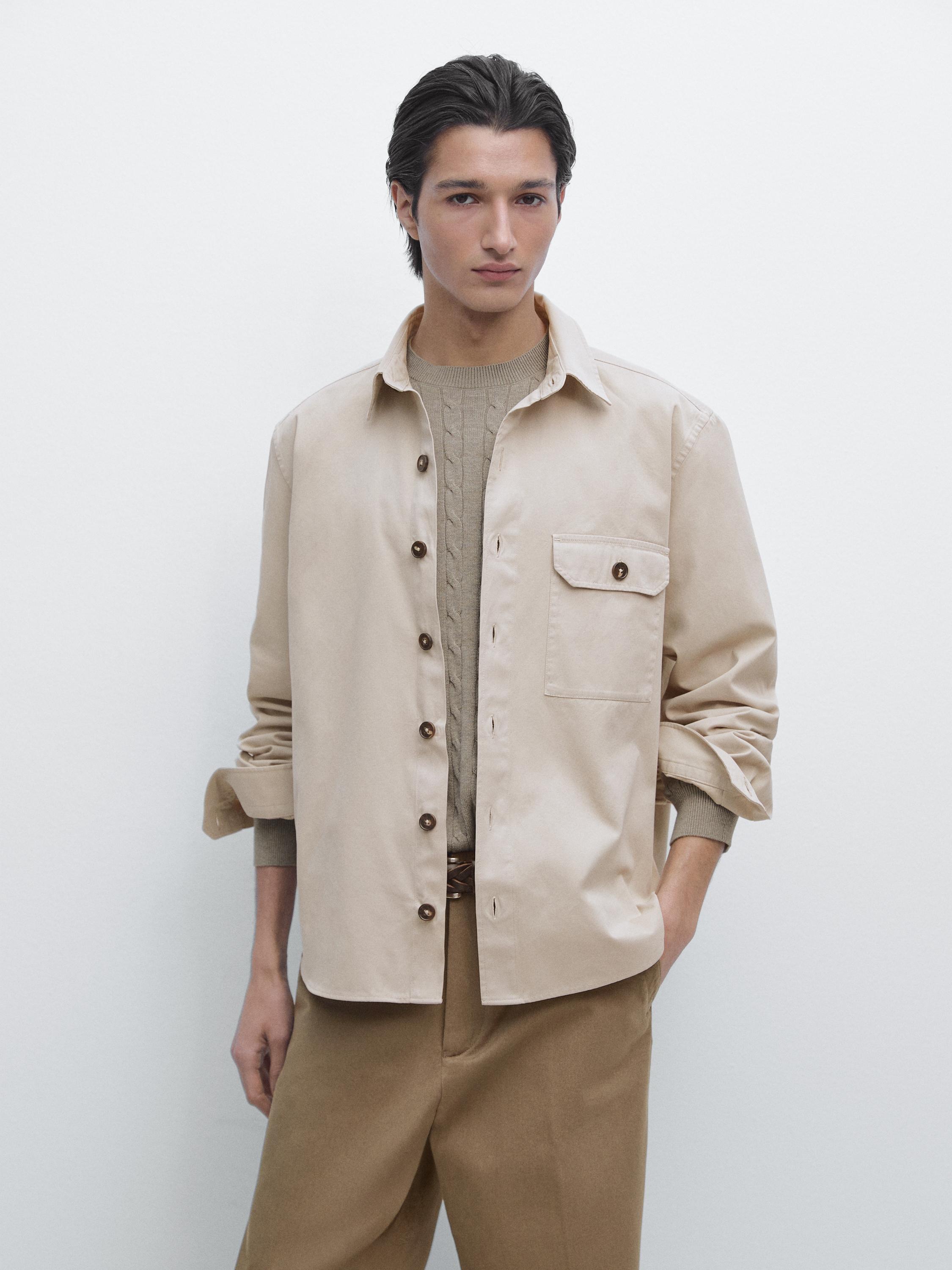 Completo di camicia-giacca beige con tasche e bottoni marroni, sopra maglione beige e pantaloni marroni.