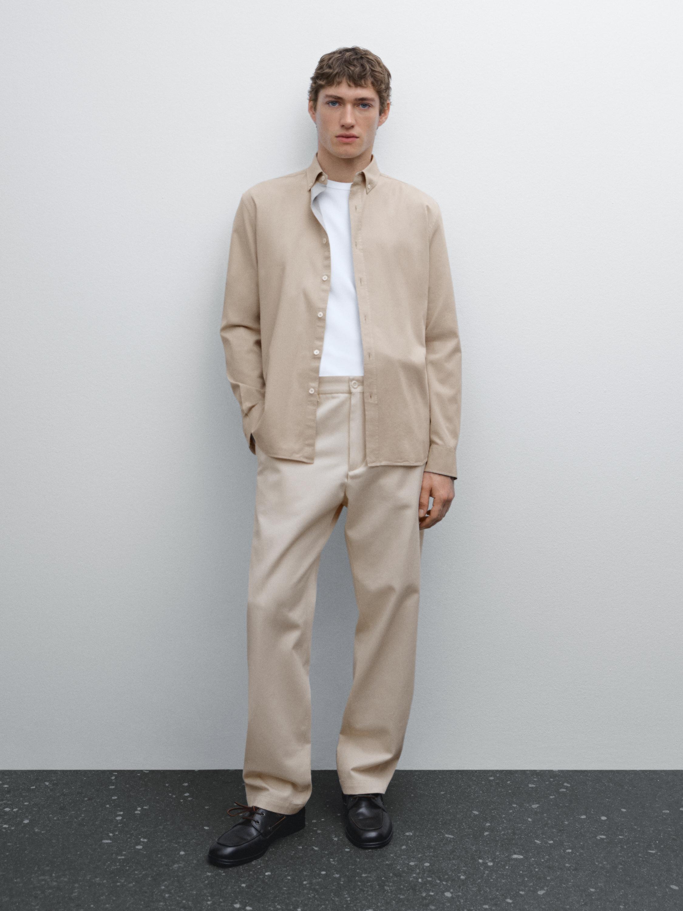 Ensemble composé d'une chemise beige et d'un pantalon beige, avec un t-shirt blanc et des chaussures noires.