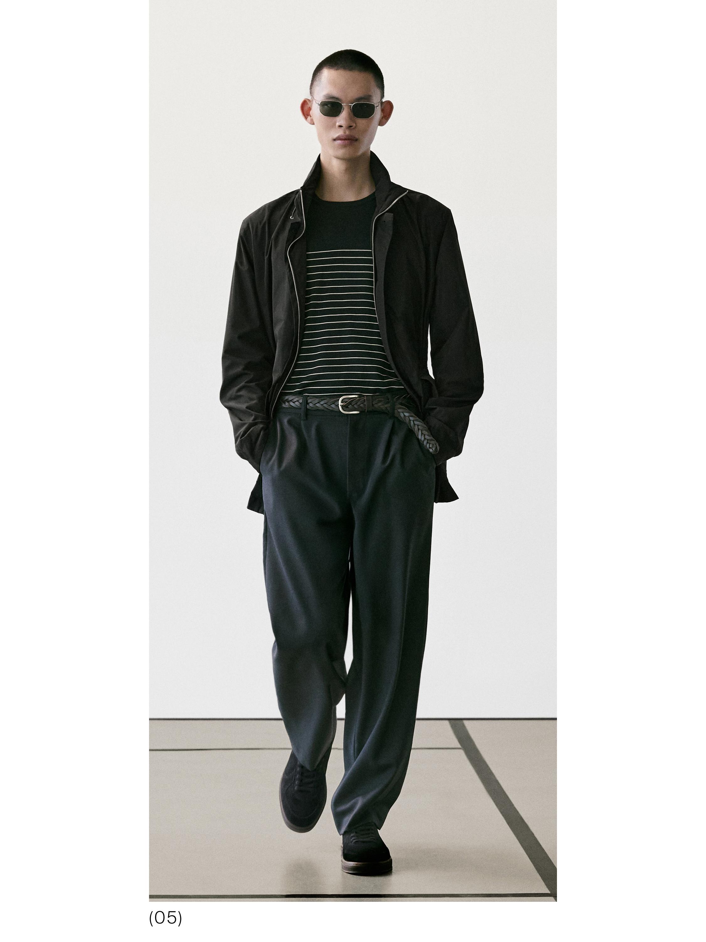 Conxunto de chaqueta negra, camiseta de raias, pantalóns escuros e cinto trenzado.