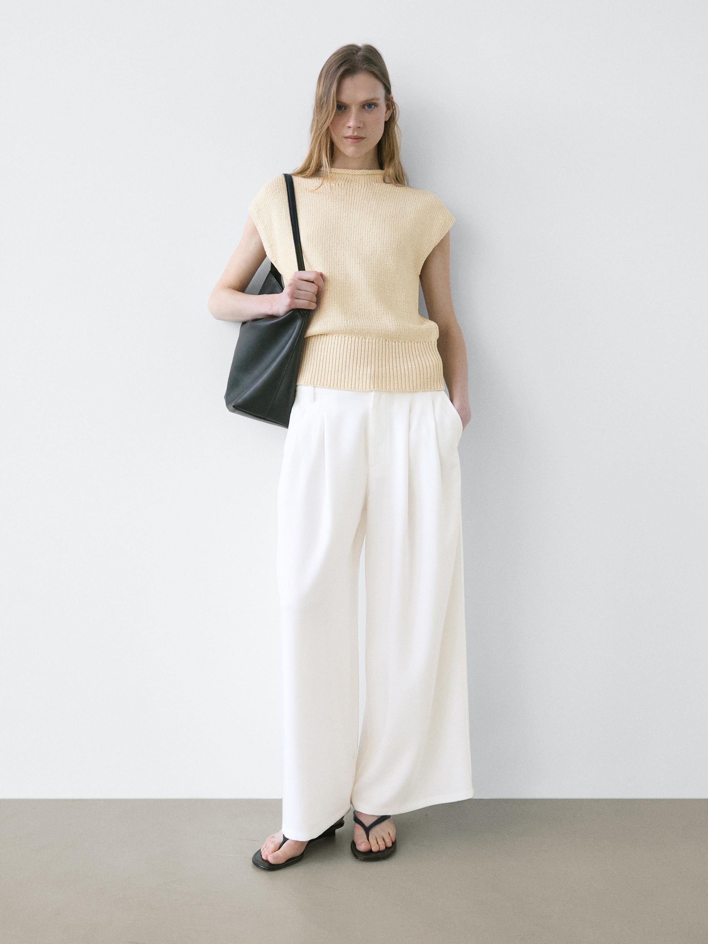 Conjunt de pantalons blancs de cama ampla amb plecs i top sense mànigues beix. Butxaques laterals visibles.